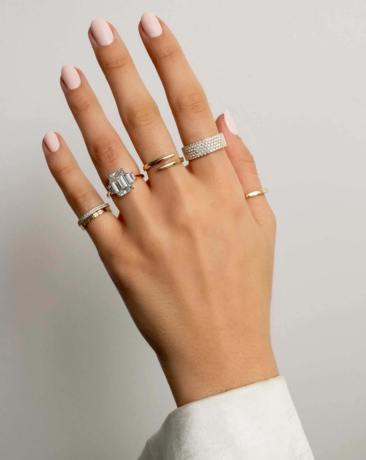 double row pave diamond ring, gold geometric stackable band, emerald-cut diamond engagement ring with side stones, gold wrap ring, five row pave diamond ring and gold band on model