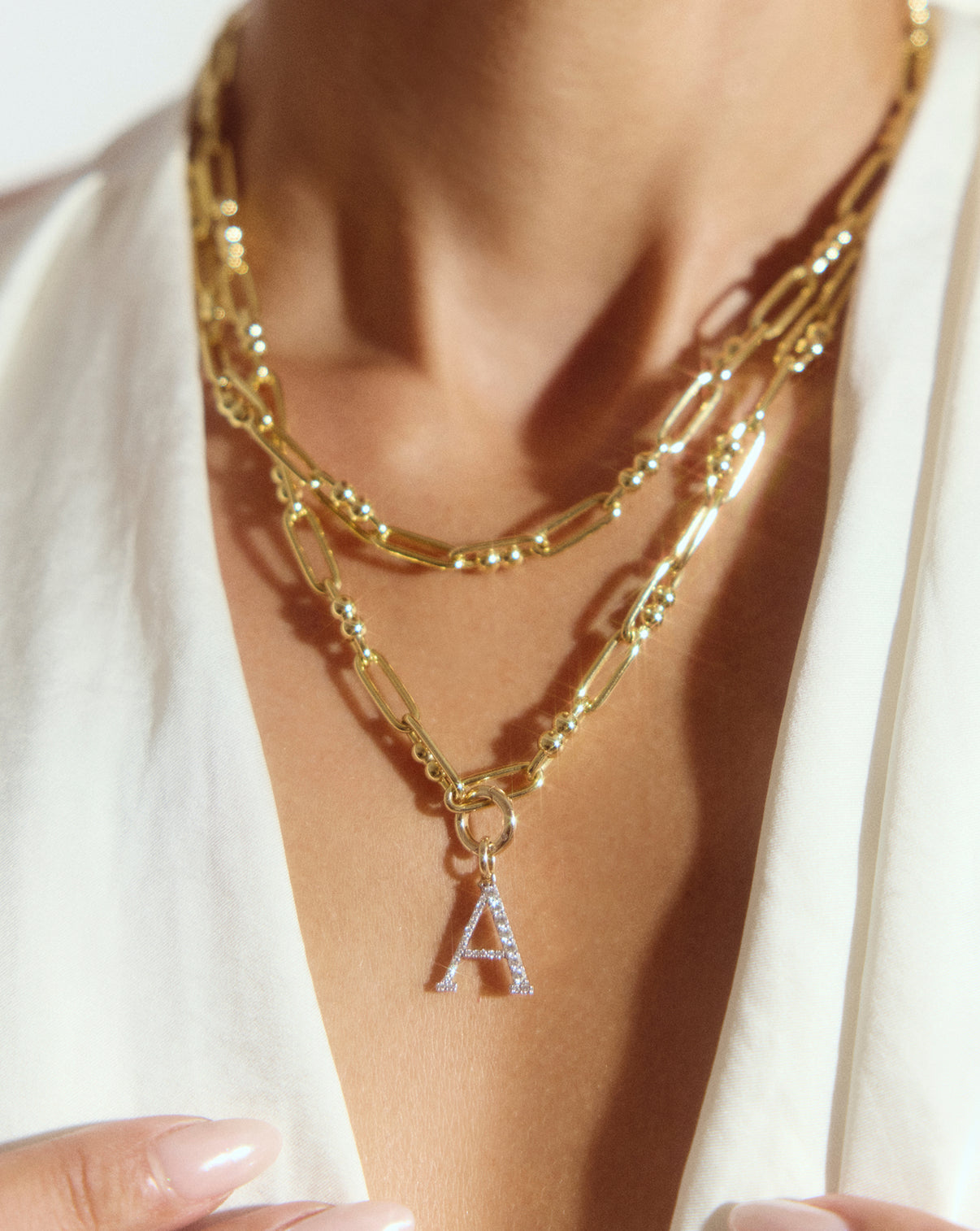 model wearing gold necklace with clique clasp and diamond letter pendant stacked with another gold necklace