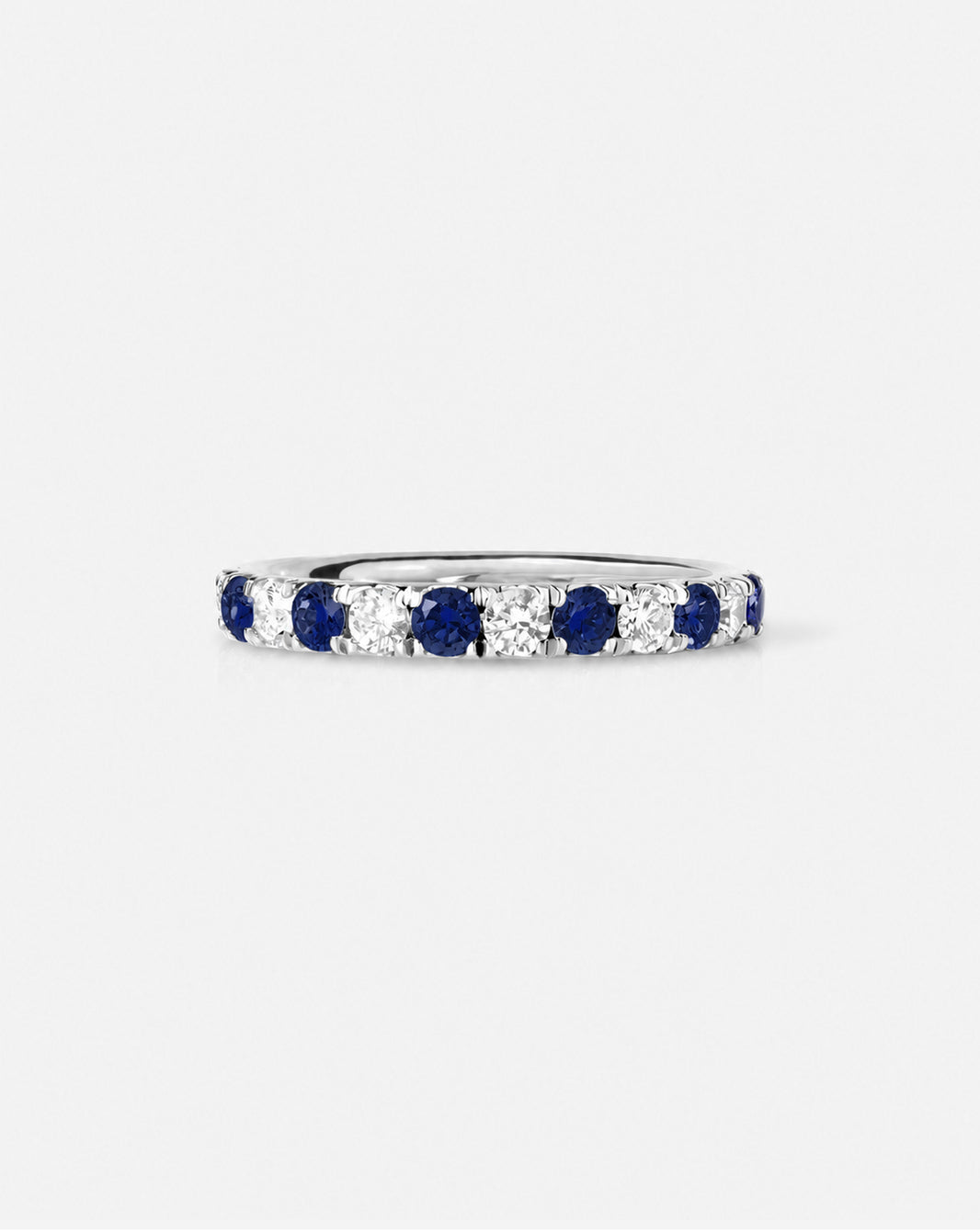 An eternity ring featuring alternating round-cut deep blue sapphires and diamonds, shown on a light gray background.