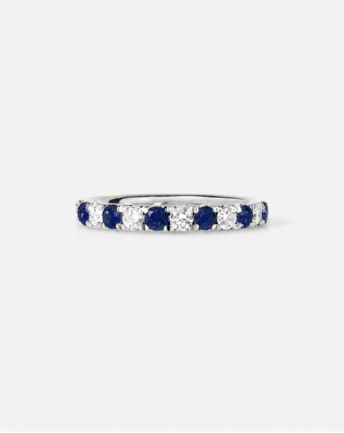 An eternity ring featuring alternating round-cut deep blue sapphires and diamonds, shown on a light gray background.