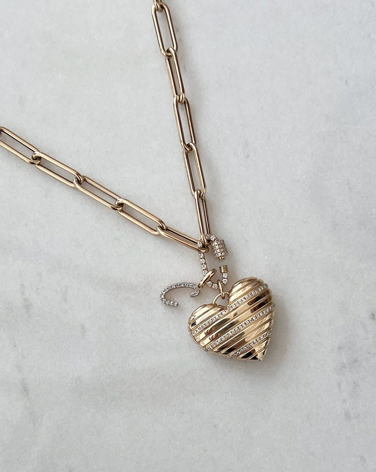 flat lay image of heart pendant with chain in yellow gold and script initial pendant