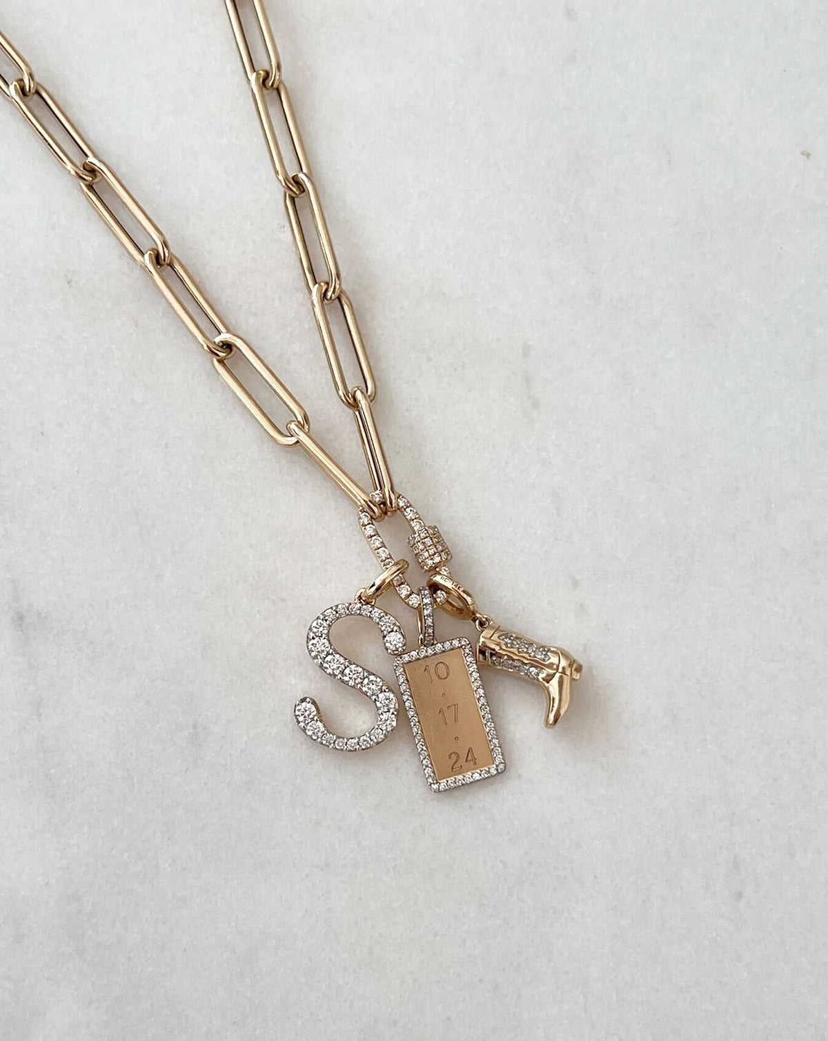flat lay image of heart pendant with chain in yellow gold and other charms stacked together