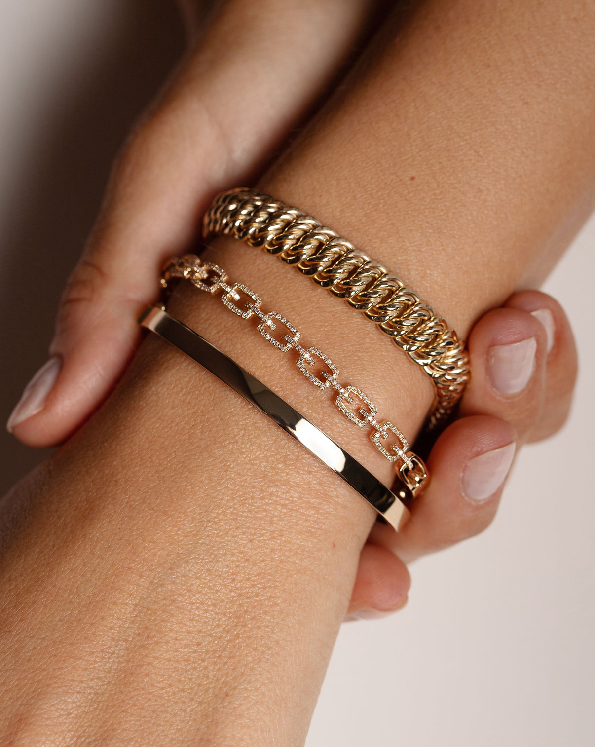 14k yellow gold bangle, diamond link bangle, and gold braided bracelet show on model