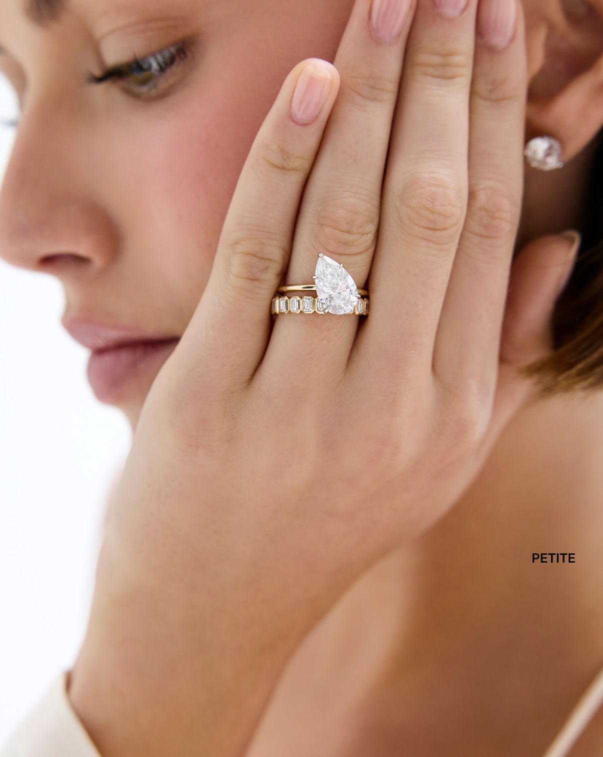 model wearing petite 2 carat weight Diamond Emerald Bezel Band in 14K Yellow Gold stacked with off-center Pear shaped Engagement Ring set in Whisper Thin global