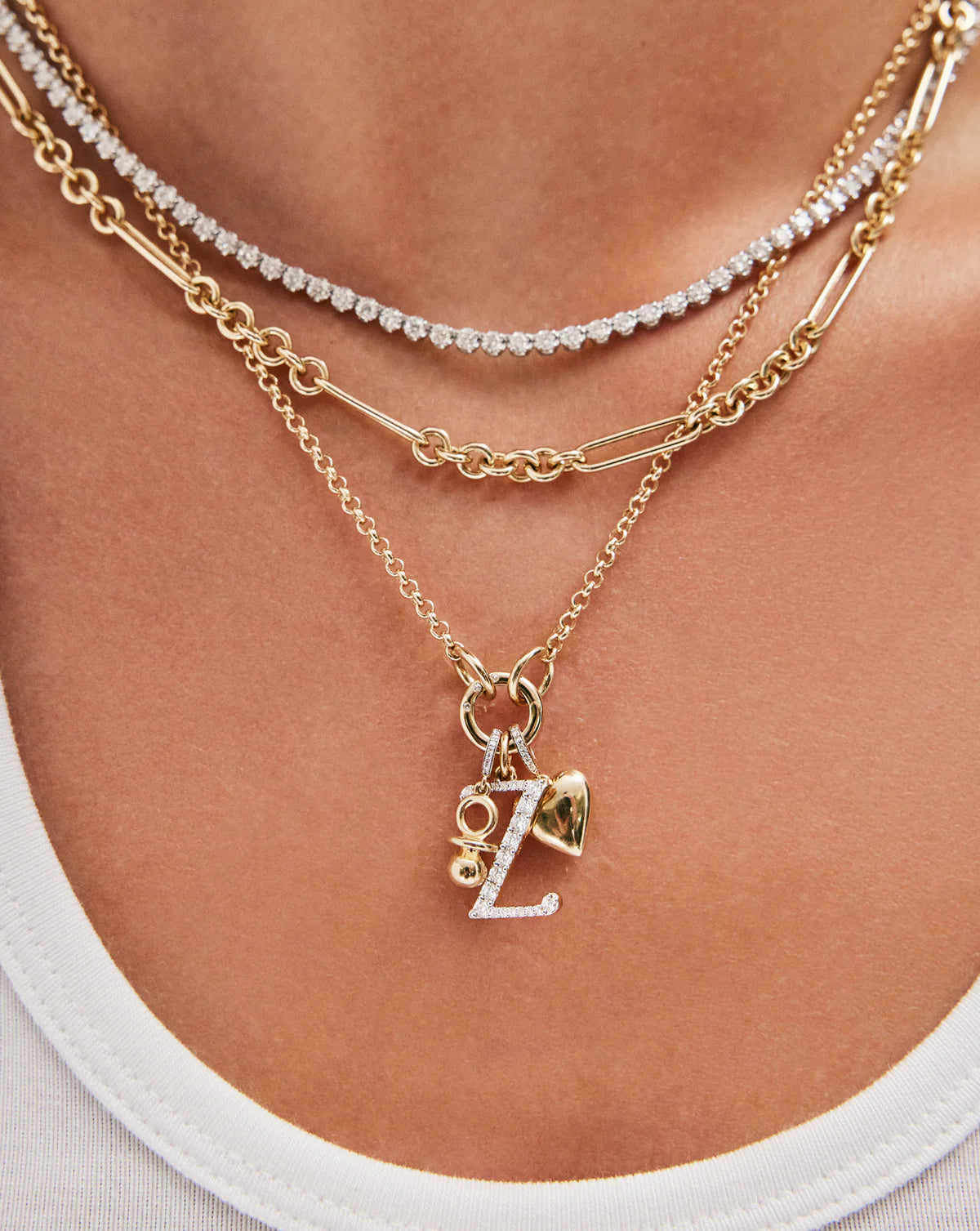 model wearing thin gold necklace with clique clasp and charm pendants, styled with other gold and diamond necklaces
