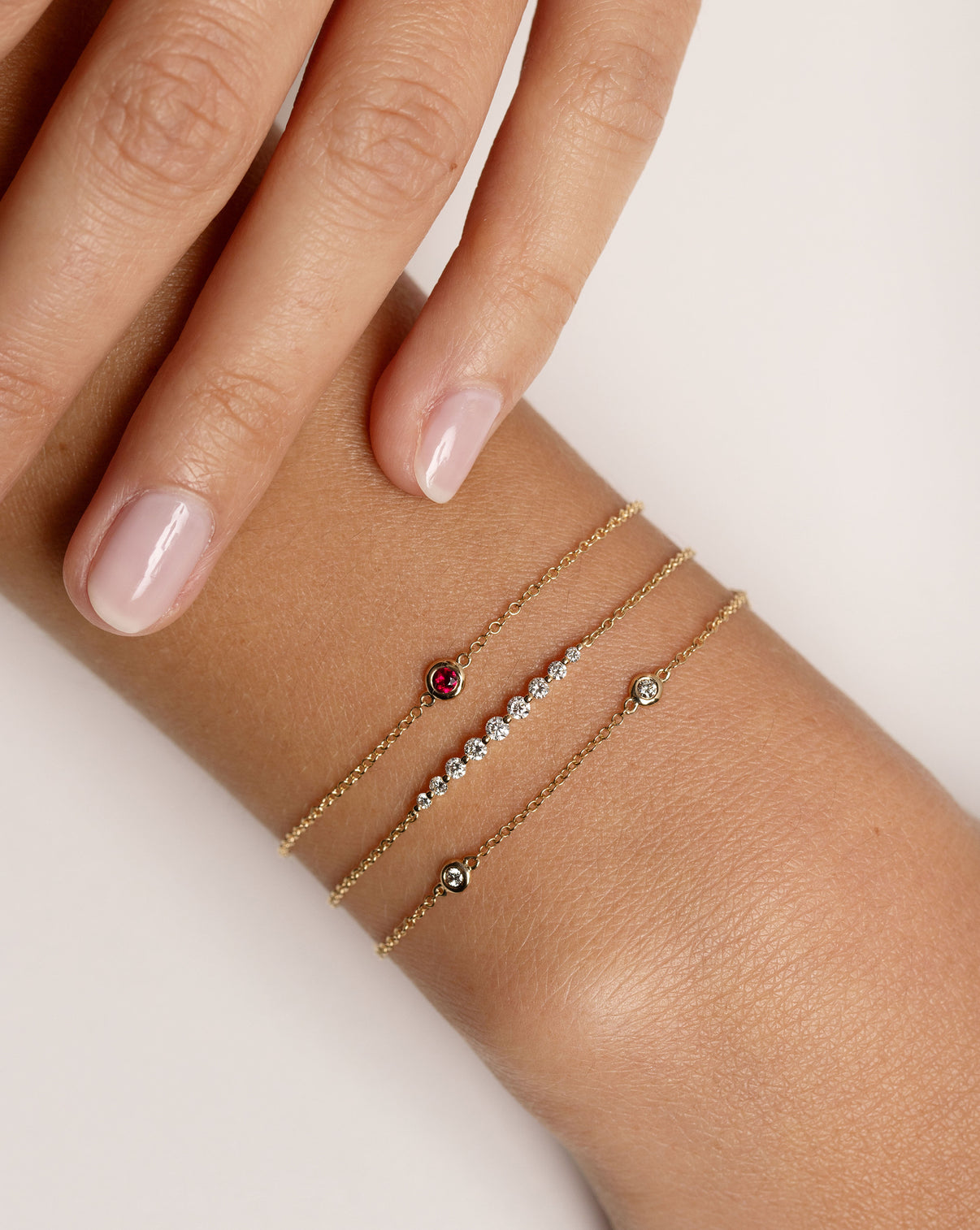 bezel-set ruby bracelet with gold chain, graduated diamonds on chain bracelet, and bezel-set round diamond station bracelet shown on model - global