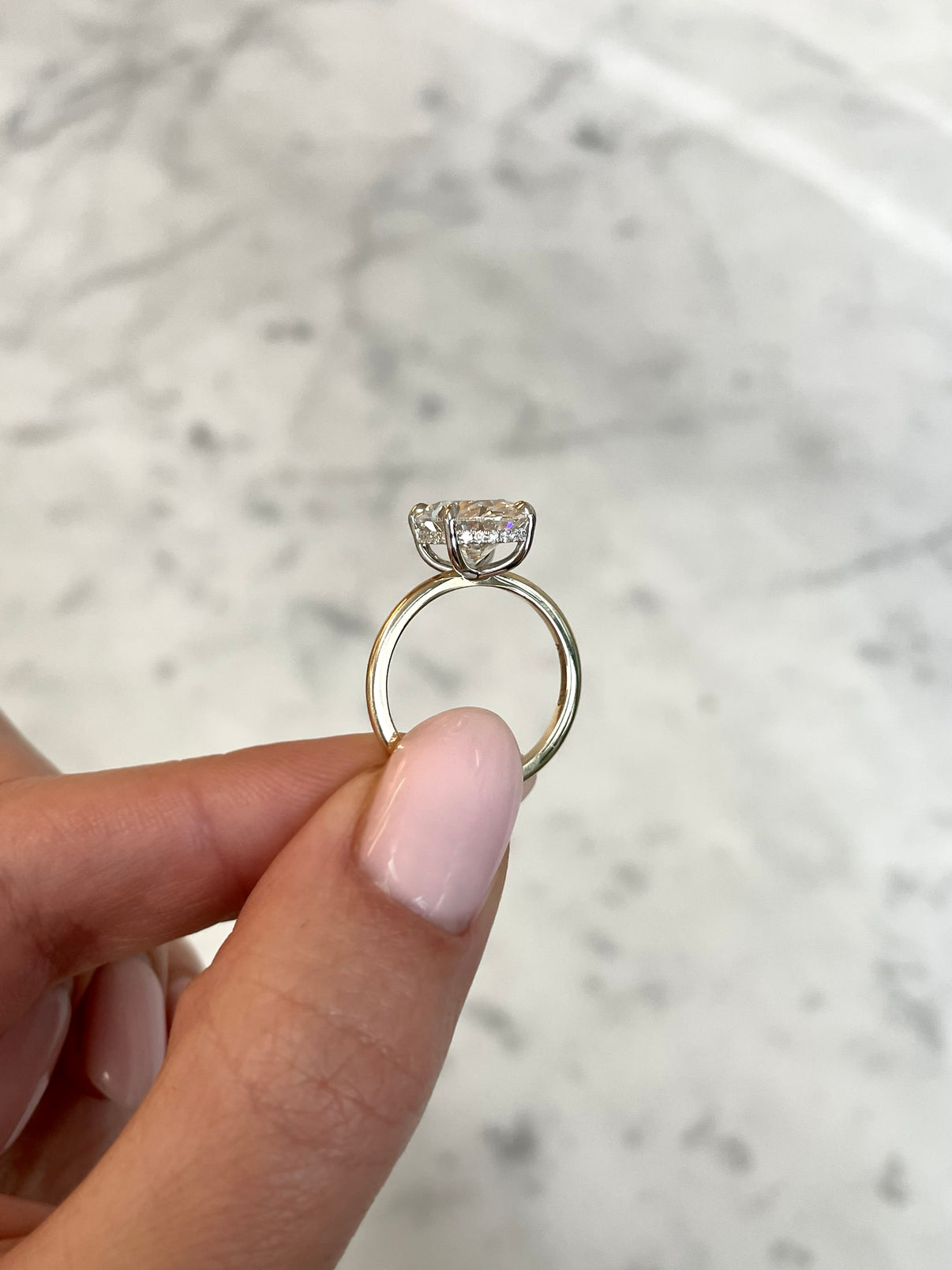 on hand of 4ct oval cut diamond in our whisper thin with hidden halo yellow gold with platinum prongs