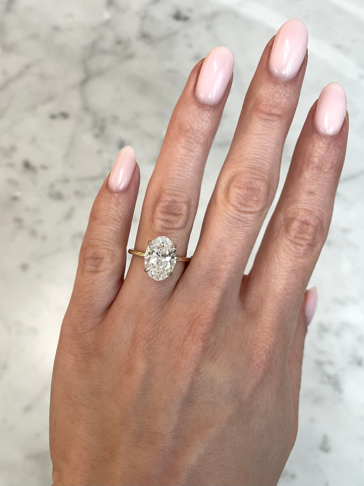 on hand of 4ct oval cut diamond in our whisper thin yellow gold with platinum prongs