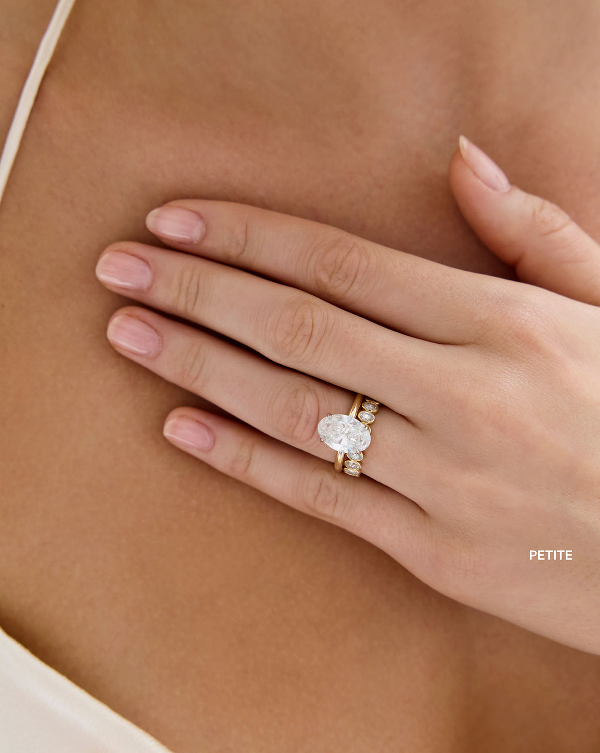 Model wearing Petite Oval Diamond Bezel Eternity Band in 14k Yellow Gold stacked with Oval Engagement Ring set in Whisper Thin Global