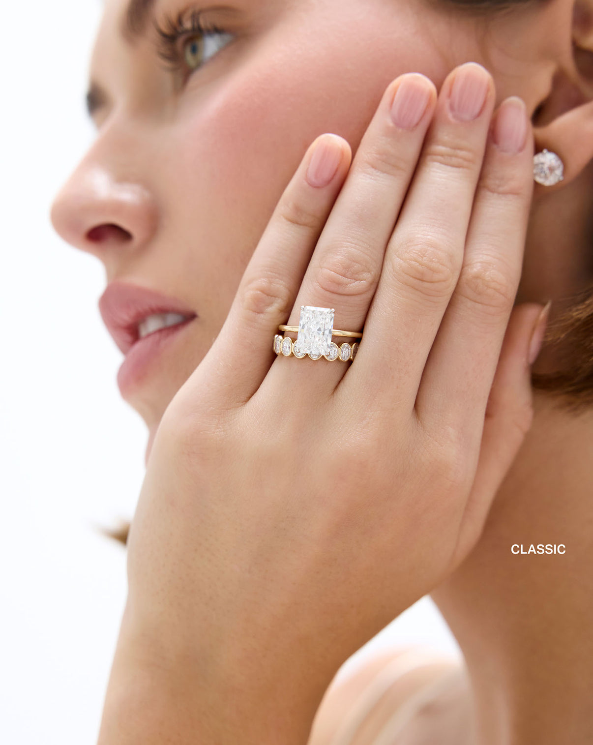 Model wearing Classic Oval Diamond Bezel Eternity Band in 14k Yellow Gold stacked with Radiant Engagement Ring set in Whisper Thin Global