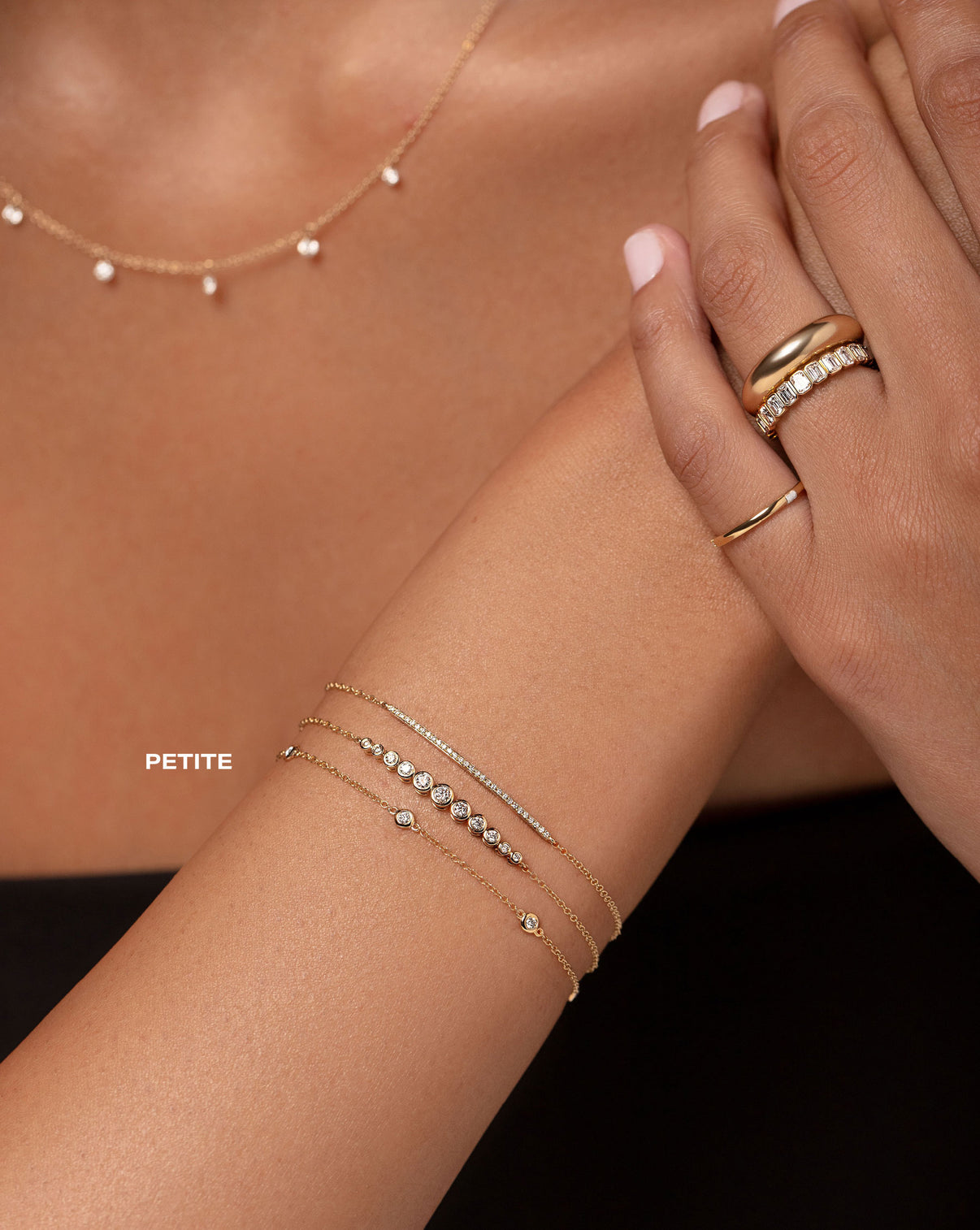 floating diamond necklace, petite bezel-set round diamond station bracelet, bezel-set round graduated diamond bracelet, diamond bar bracelet, gold pinky ring, bezel-set emerald diamond eternity band, and gold cloud ring show on model PETITE