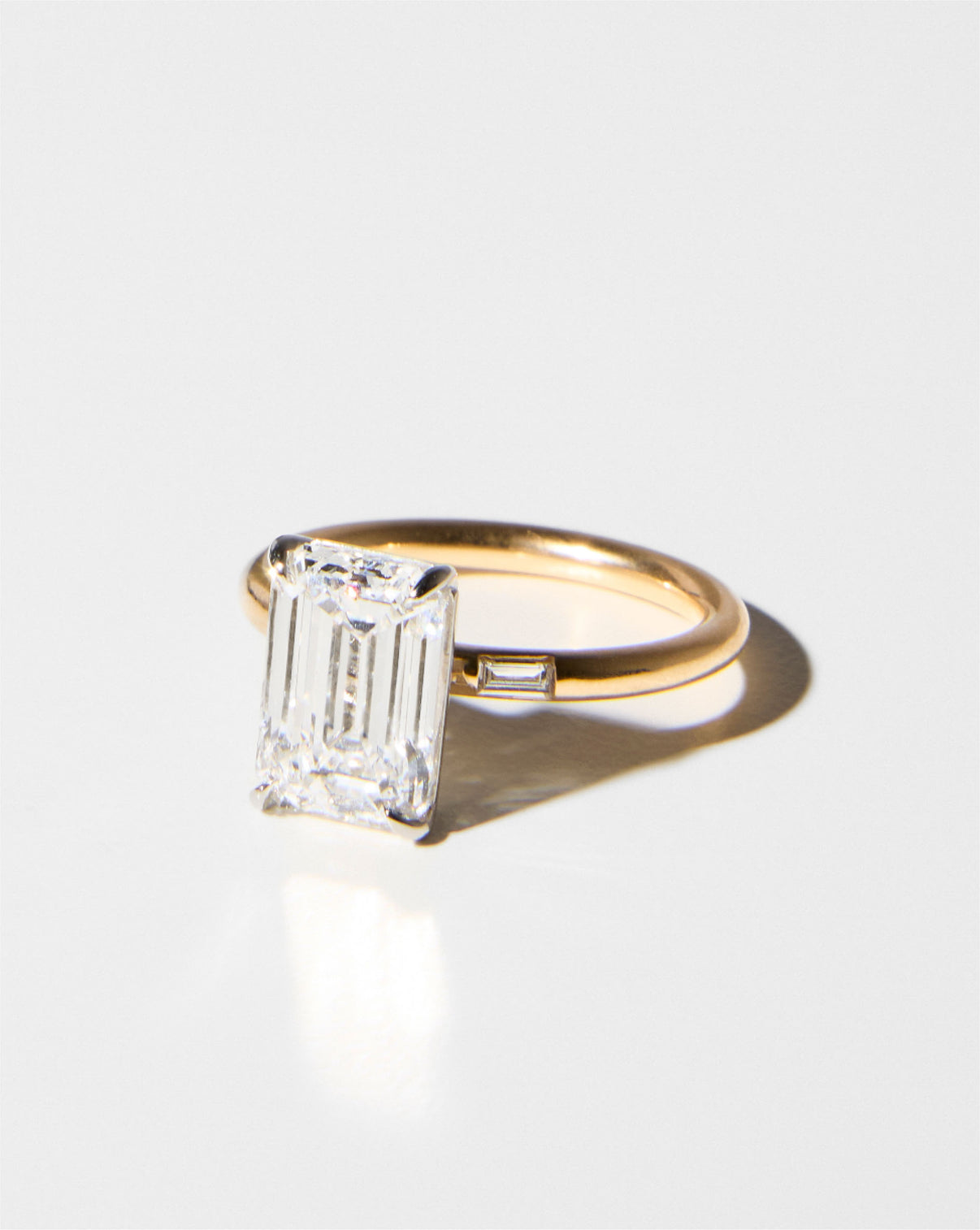 3 carat Emerald Diamond Engagement Ring in Yellow Gold Cloud Three Stone with Baguettes placed against a white background