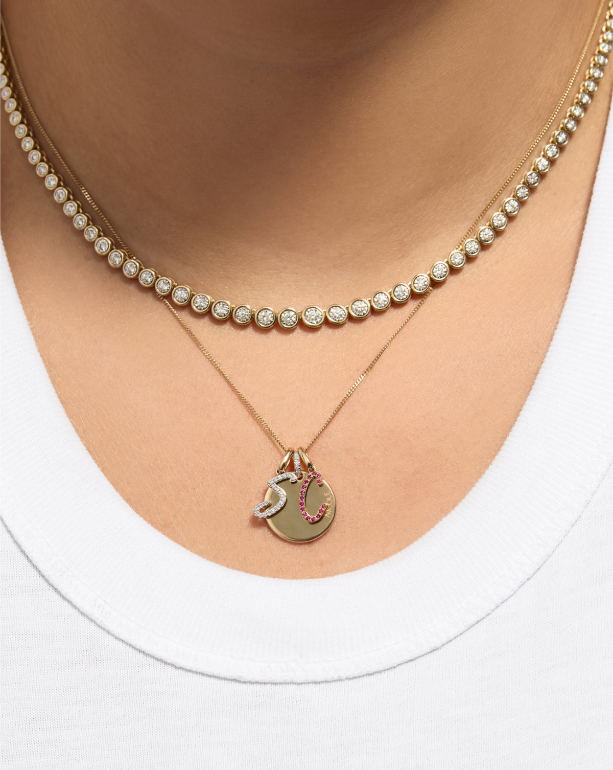 Gemstone Script Initial Necklace in ruby styled with other charms and a tennis necklace on model
