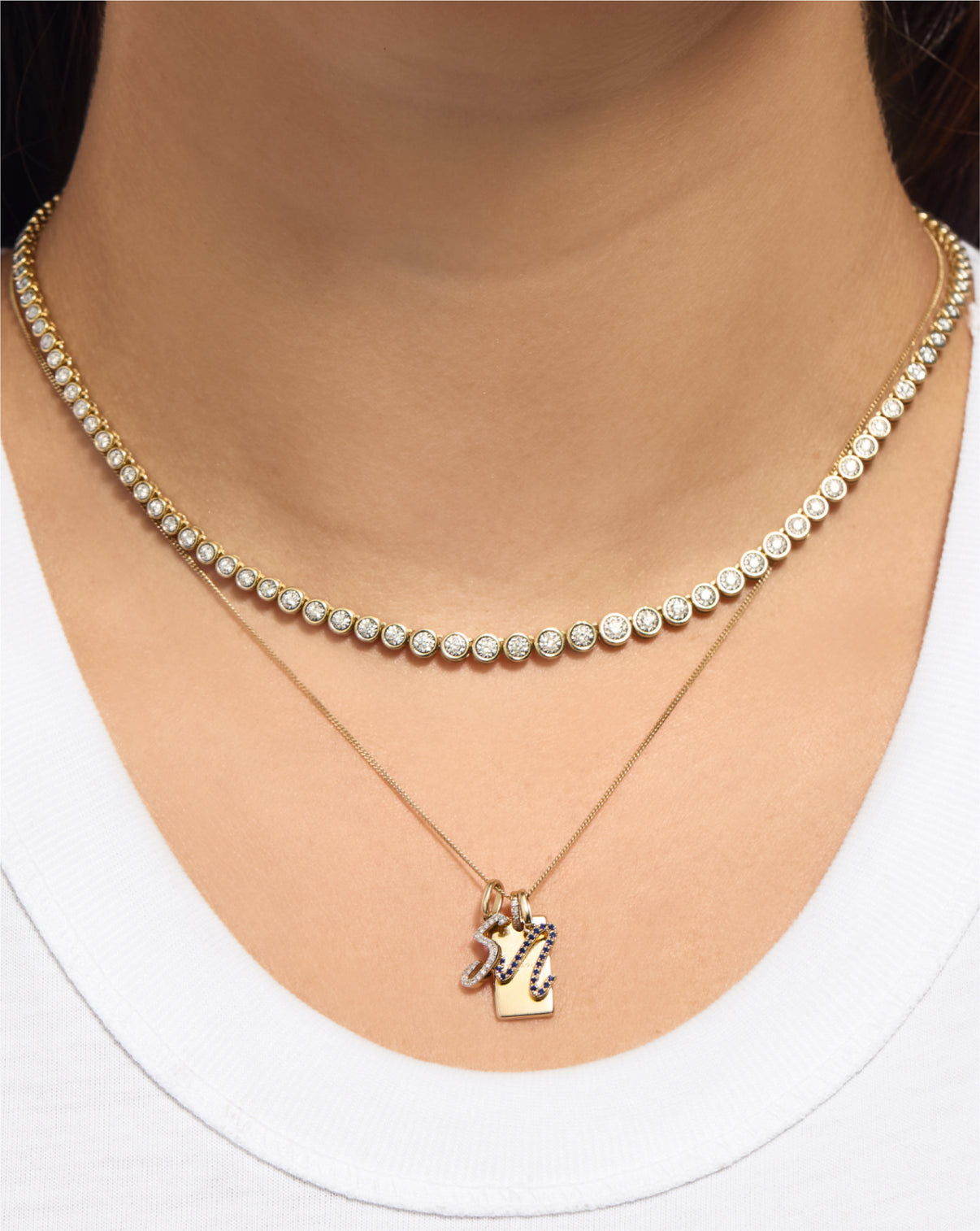 Gemstone Script Initial Necklace in sapphire stacked with other charms and a tennis necklace on model