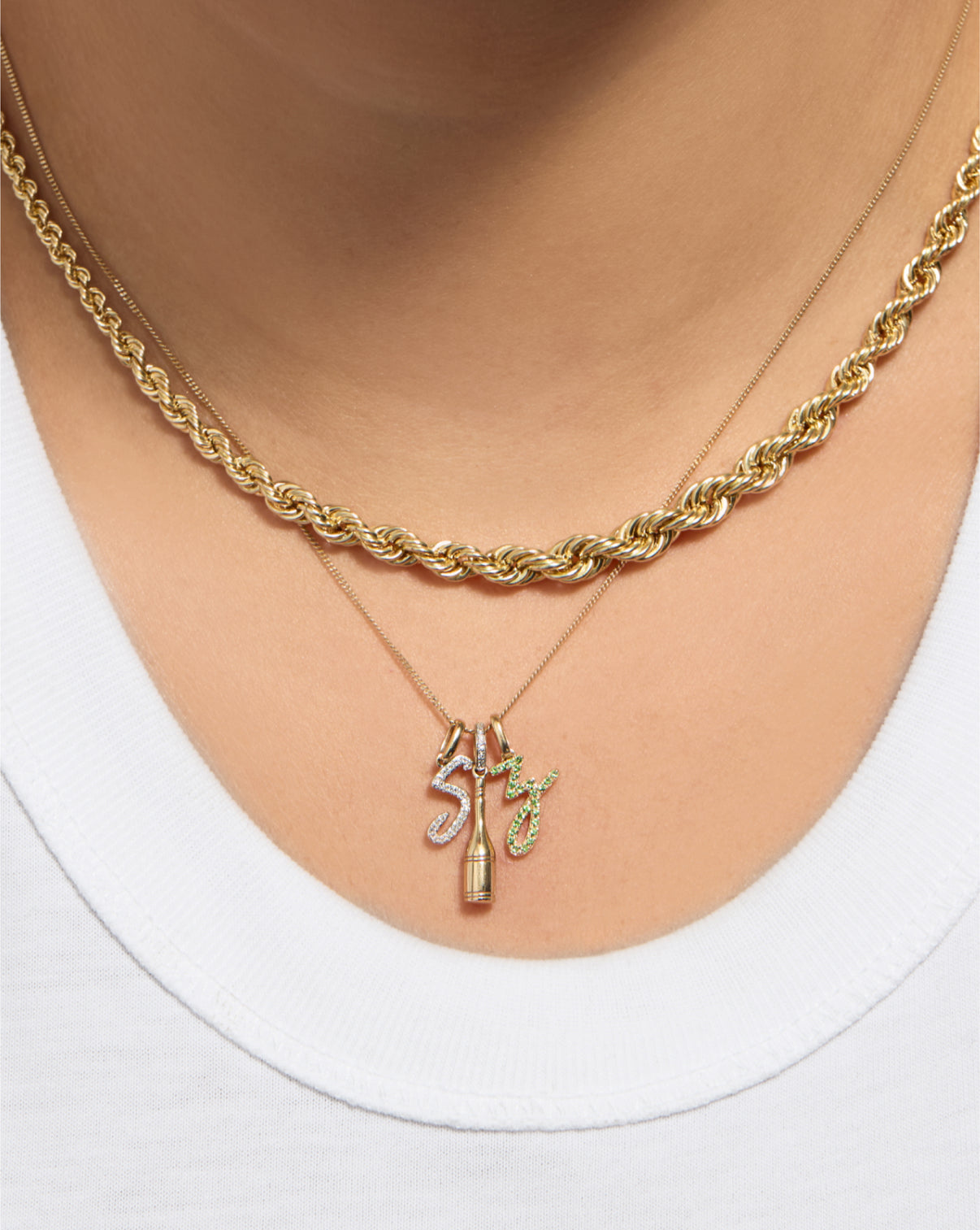 Gemstone Script Initial Necklace in green tsavorite styled with other charms and gold necklace on model