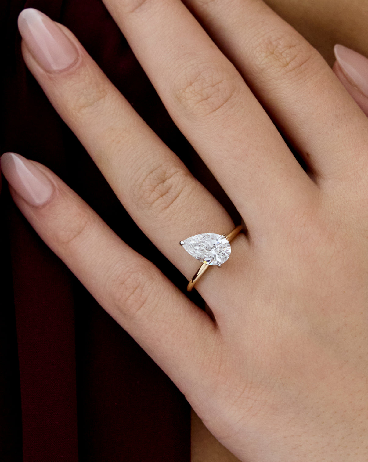 Close up of model wearing 2.15 carat Pear ring of the 5.21 Emerald & Pear Whisper Thin® Duet diamond Engagement ring in 14K Yellow Gold