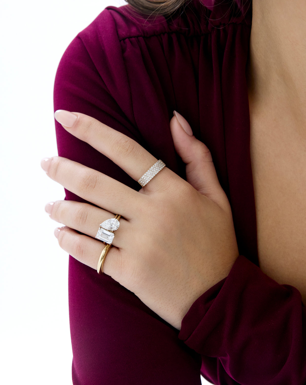 model wearing the stacked 5.21 Emerald & Pear Whisper Thin® Duet diamond Engagement ring in 14K Yellow Gold with other diamond and gold jewelry on hand