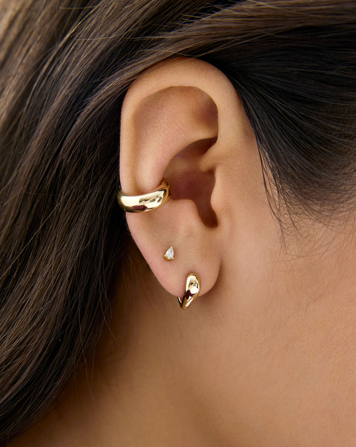 14K Yellow Gold Heart Huggie Earrings styled on model's ear with a pear diamond stud and gold ear cuff