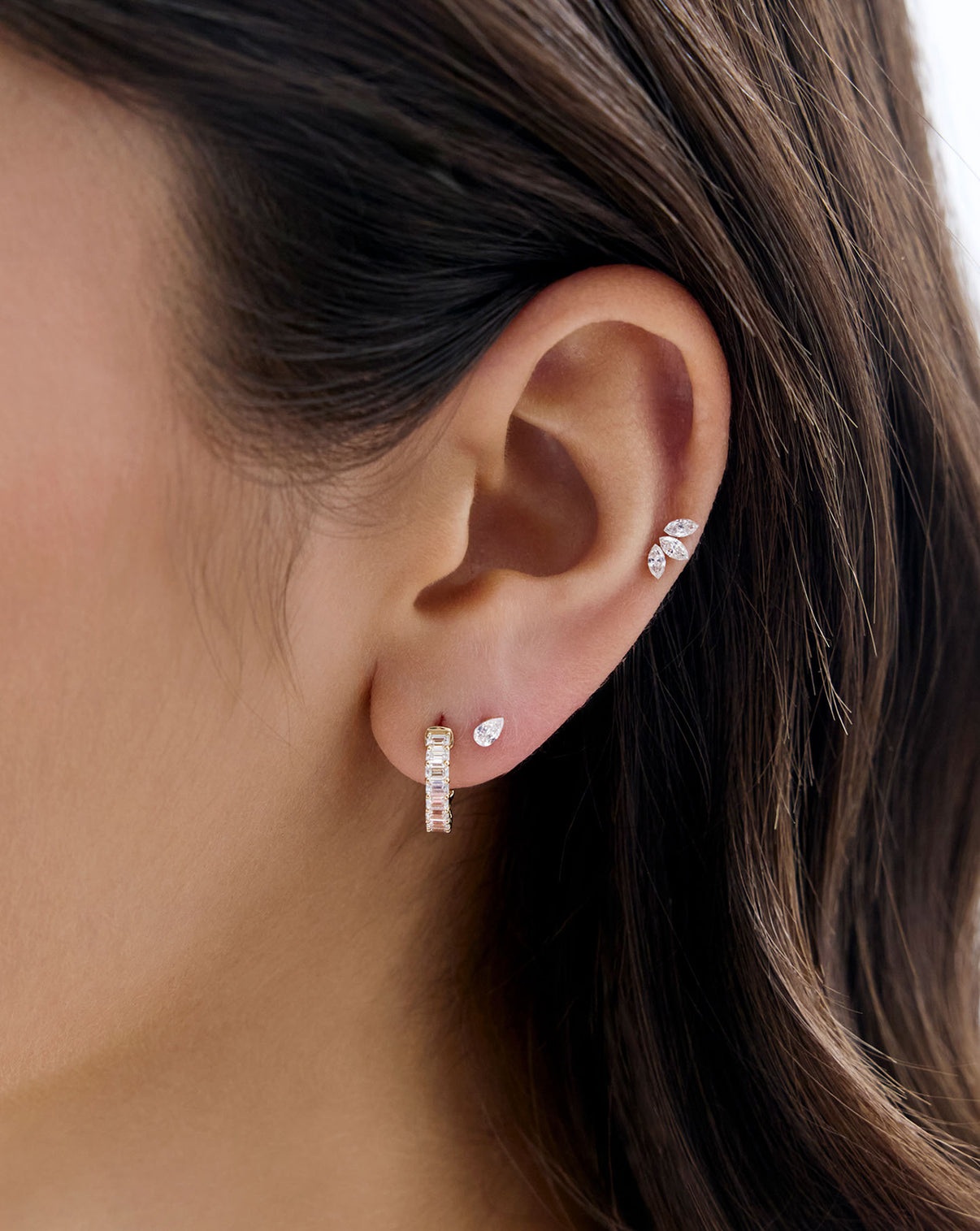 Close up image of model's ear, wearing the Marquise Lab Diamond flatback earring and styled with a diamond huggie and the Mini Pear Lab Diamond flatback earring