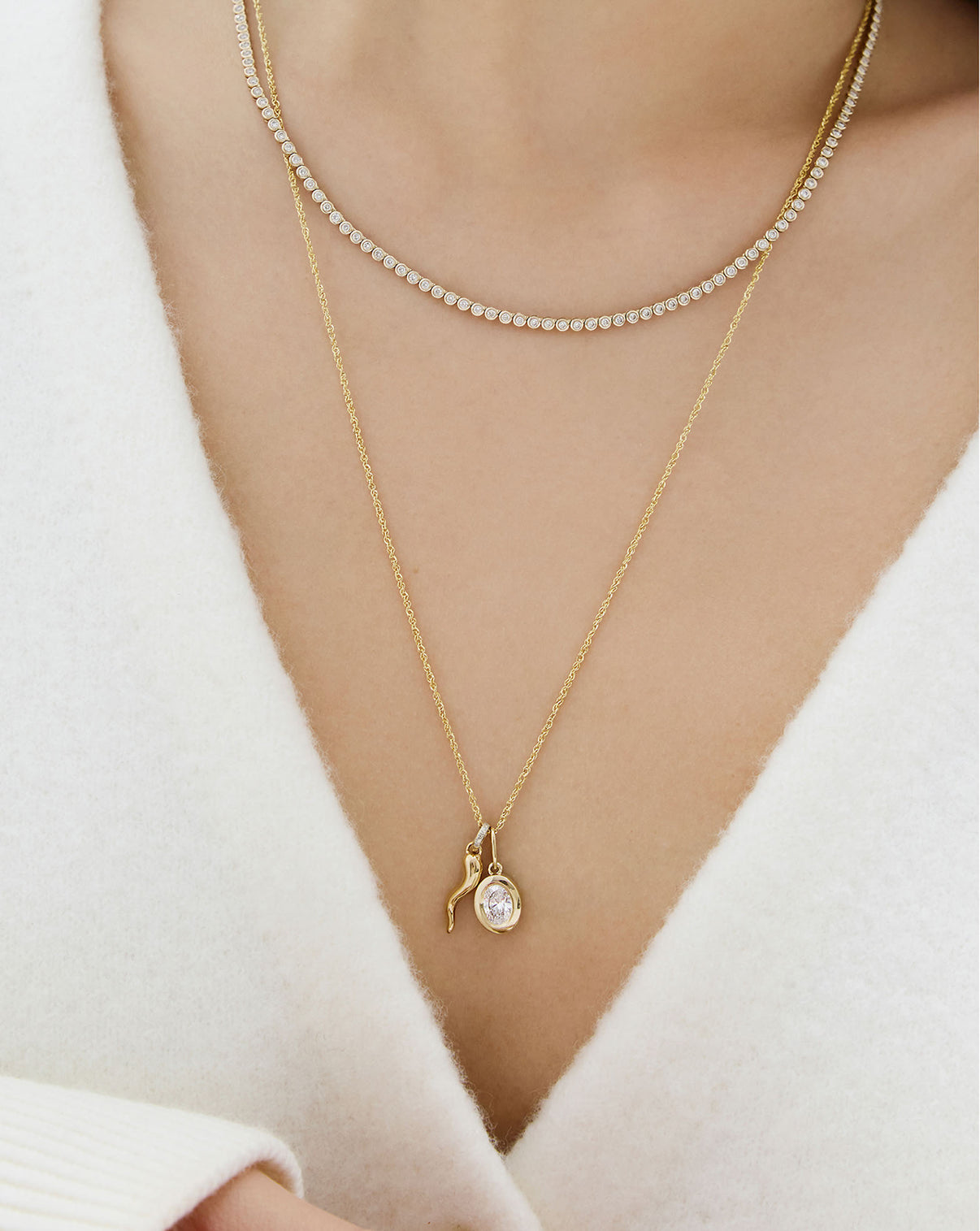 Model wearing a 14K yellow gold cornicello charm pendant necklace stacked with a framed diamond pendant and a tennis necklace