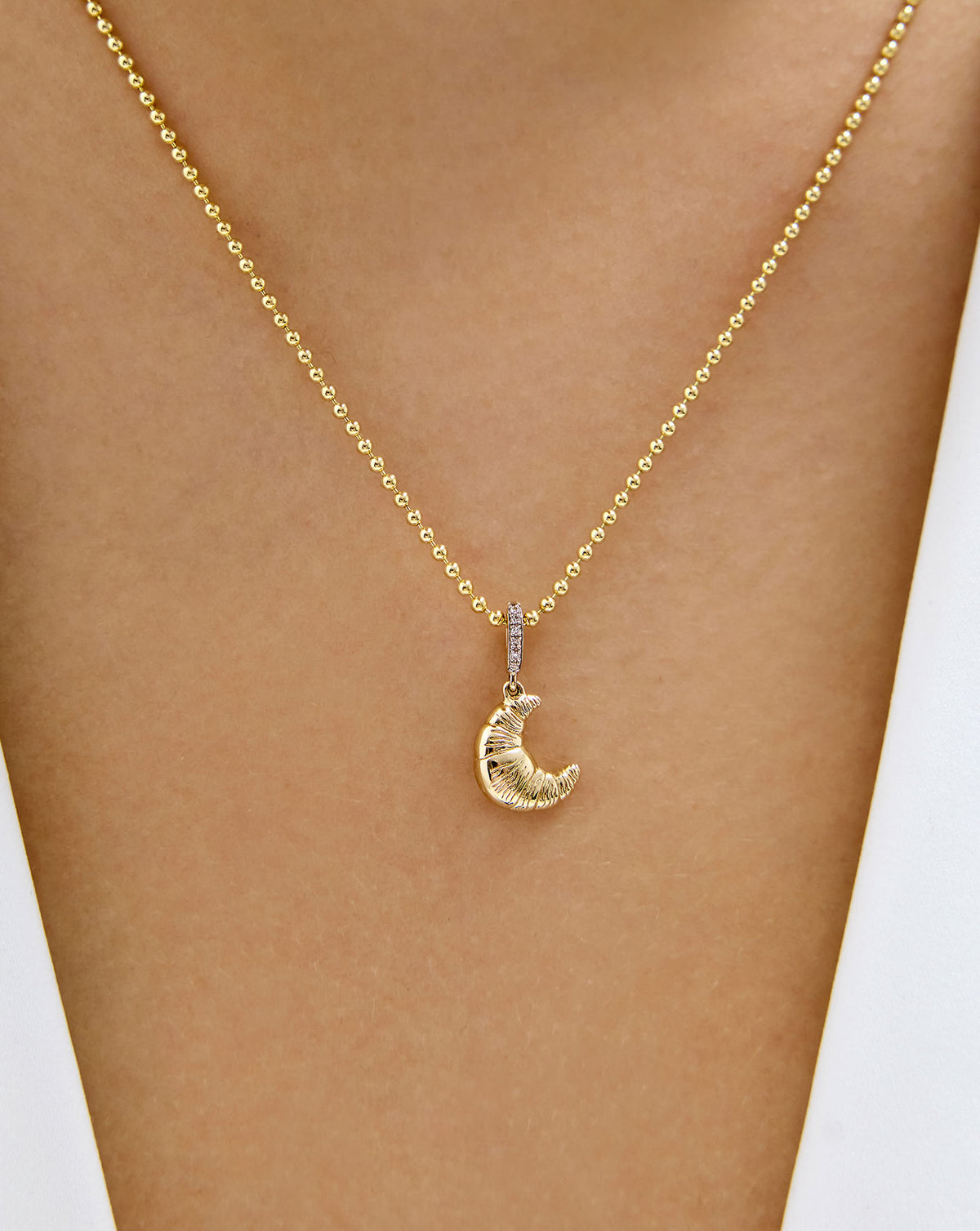 Close up of 14k yellow gold Croissant Charm worn on chain around model's neck