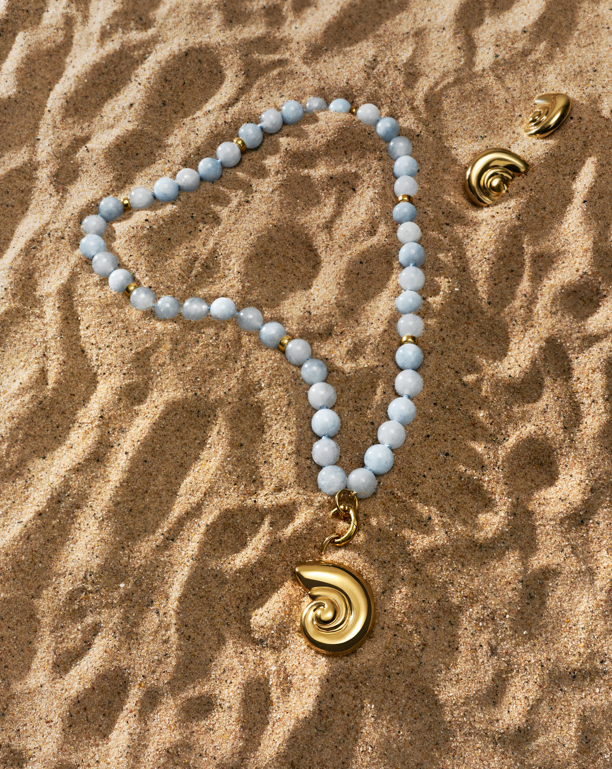 Capri Coast Aquamarine beaded necklace laying on top of sand