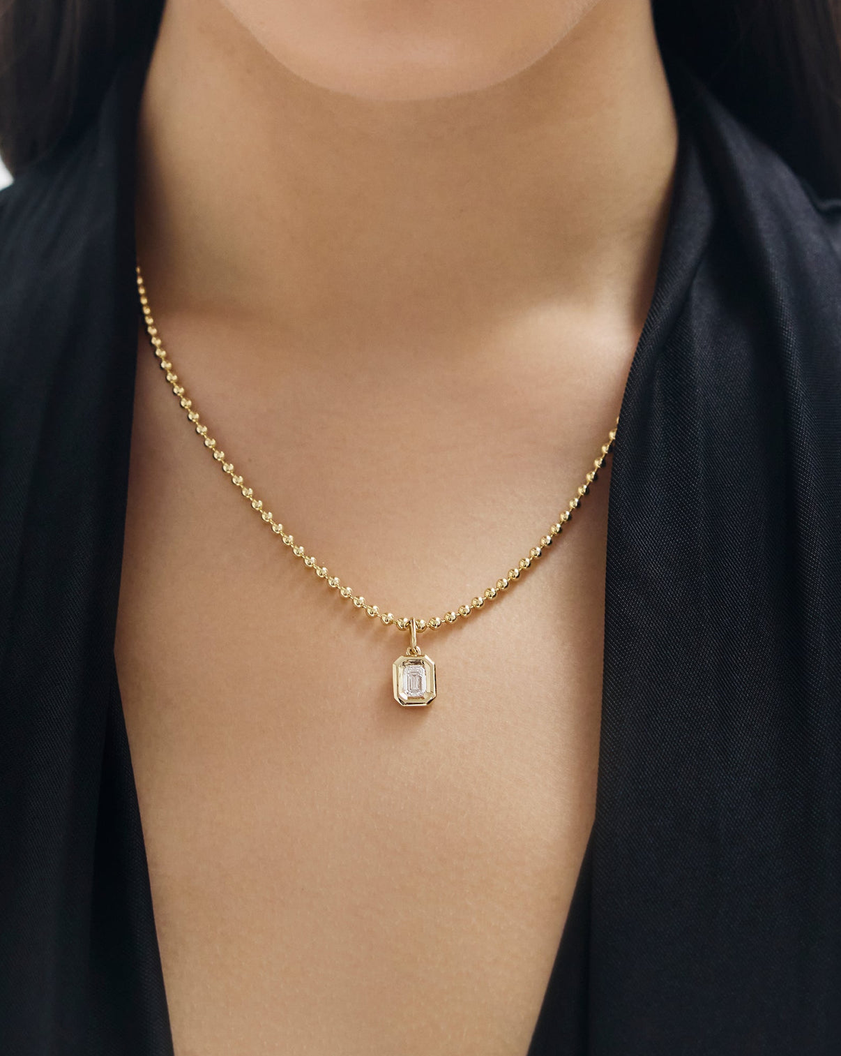 Gold necklace with a pendant on a person wearing a black top global