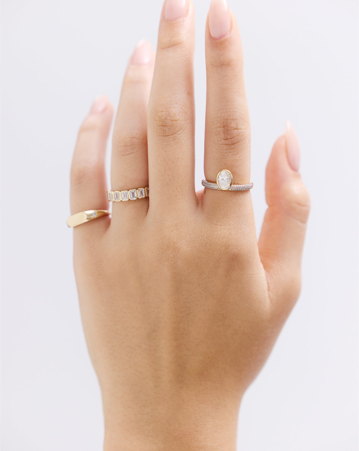 Hand wearing 14k gold oval bezel ring with pavé diamond band