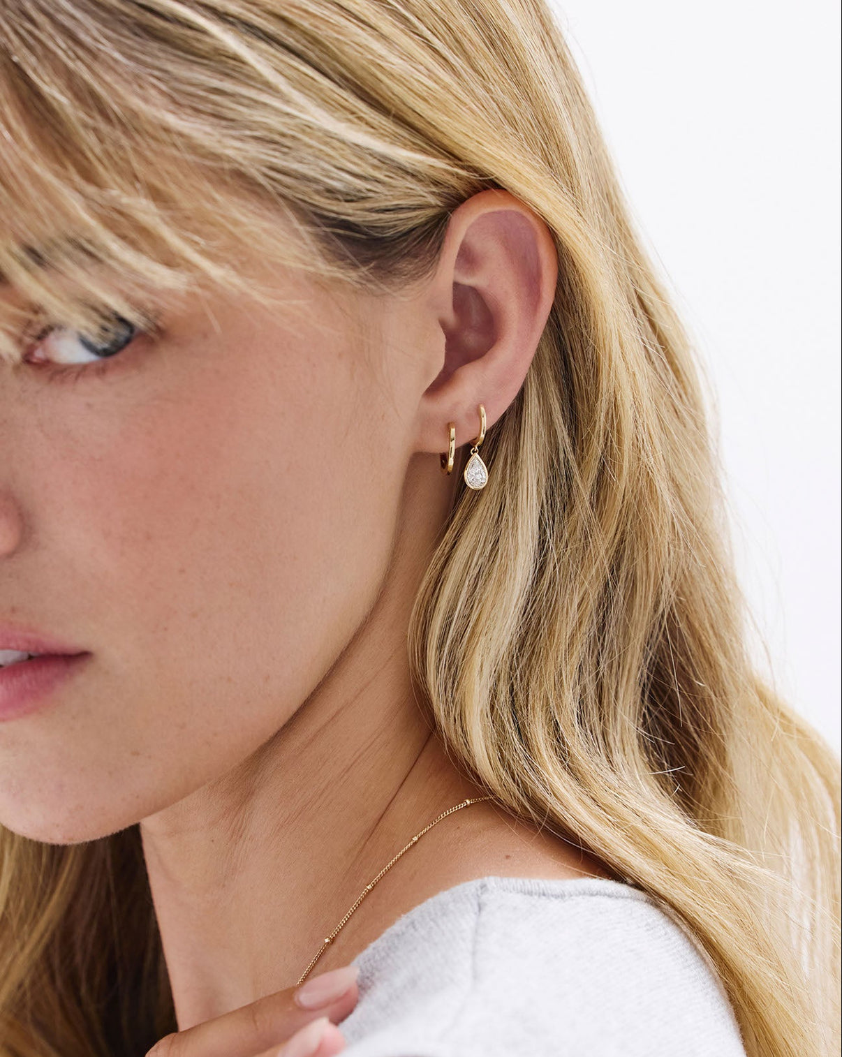 Classic Gold Huggies earrings styled with pear shaped drop earrings on model's ear