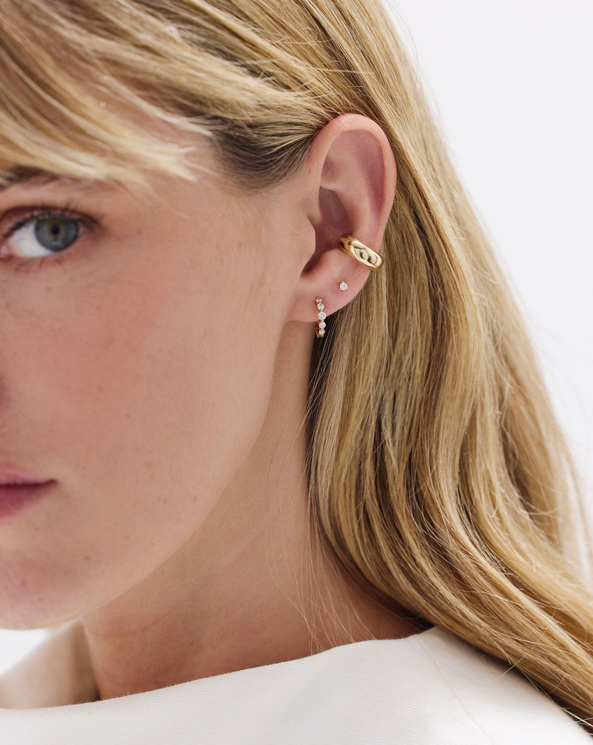 Model wearing Graduated Single Prong Diamond Huggies styled with a Diamond stud earring and Gold ear cuff