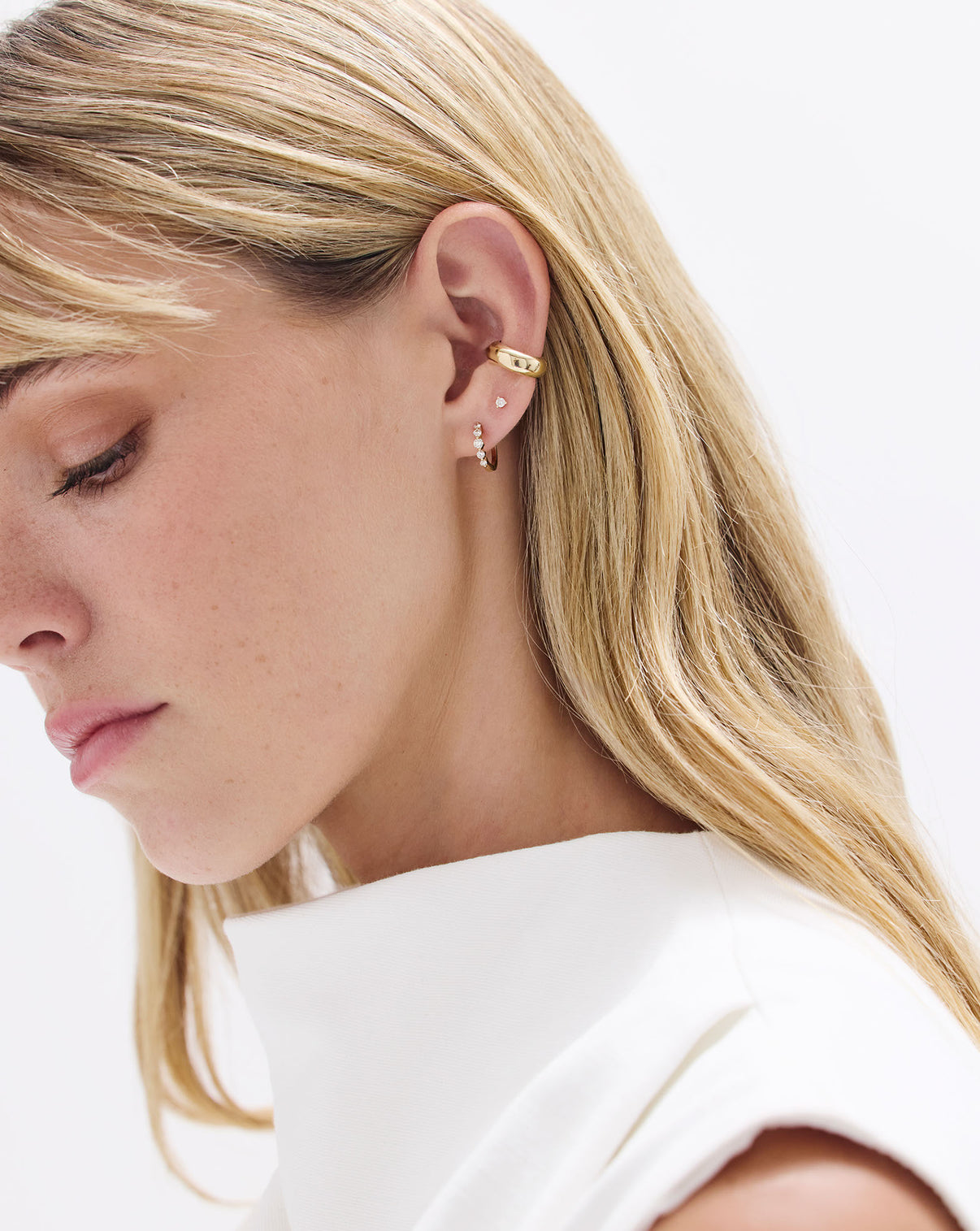 Model wearing Graduated Single Prong Diamond Huggies styled with a Diamond stud earring and Gold ear cuff