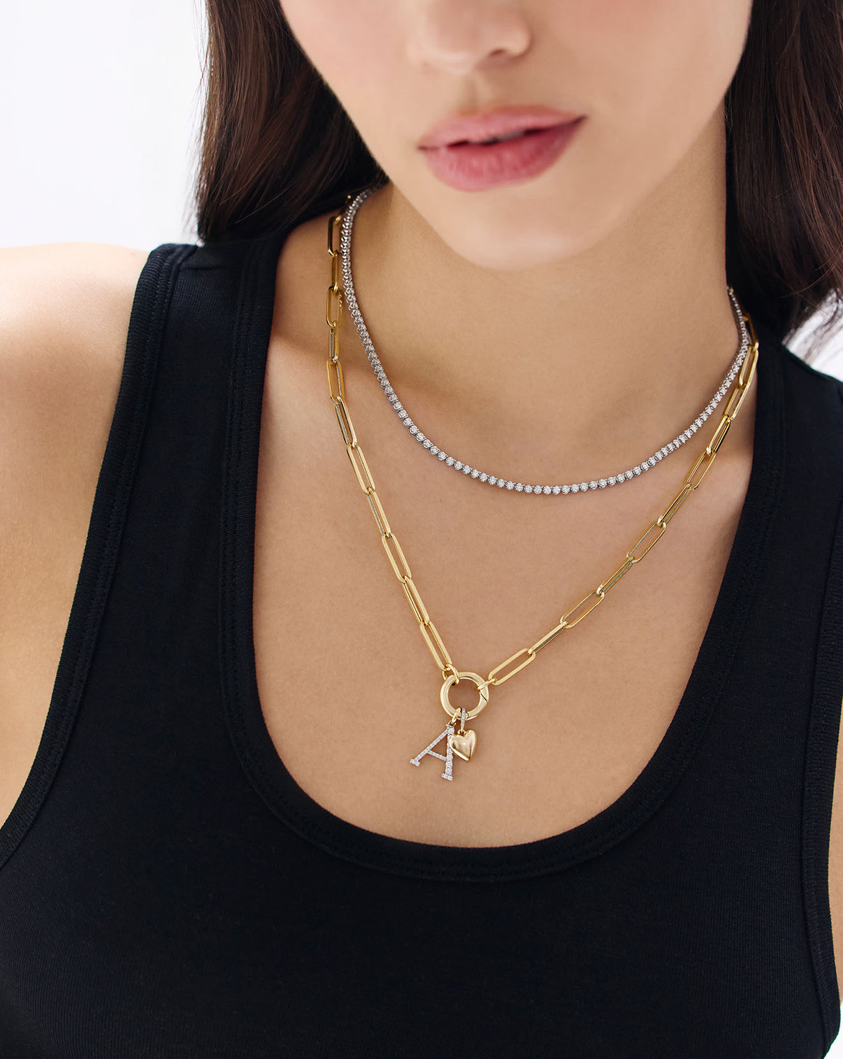 gold necklace with heart charm and letter pendant shown on model's neck along with a diamond necklace