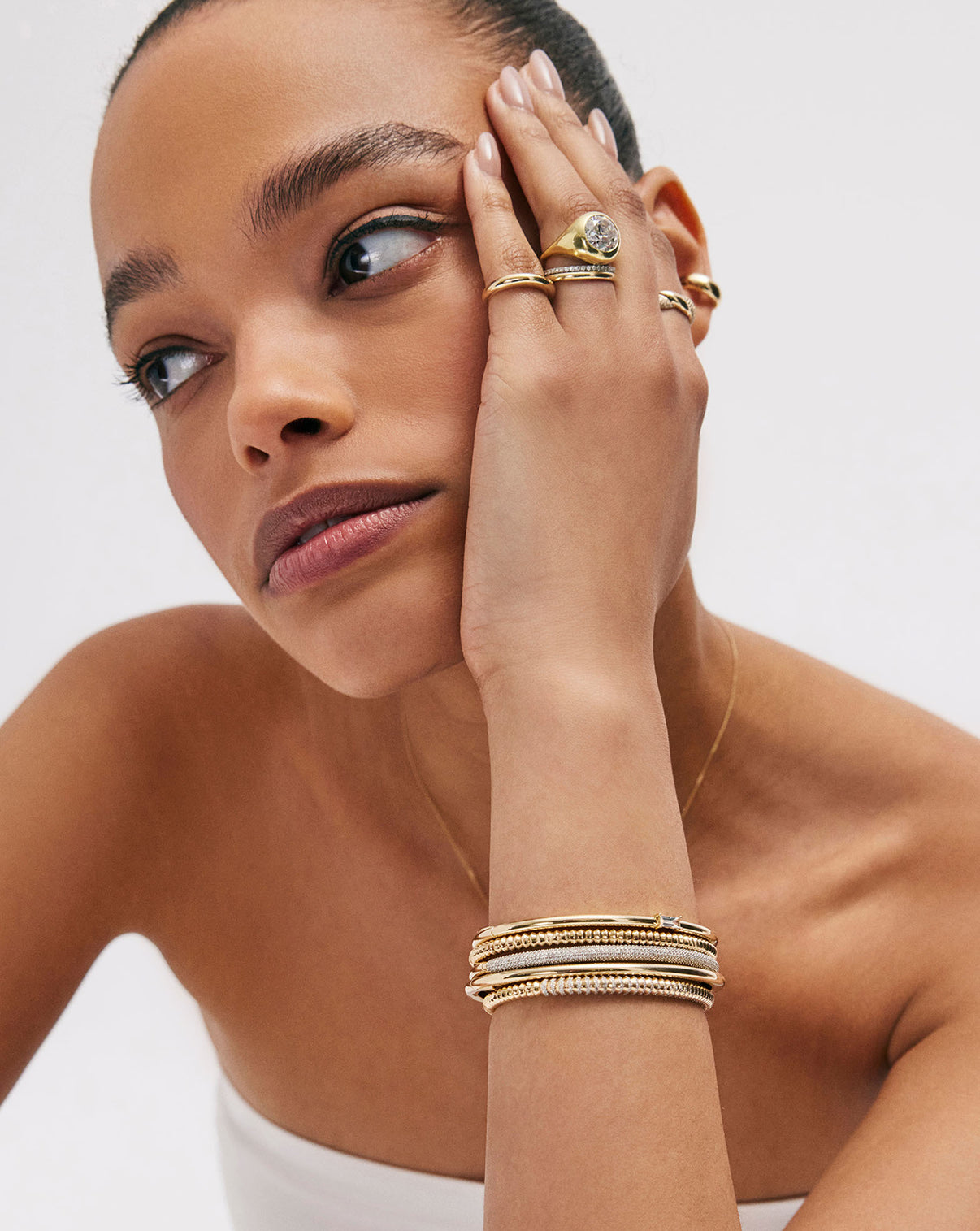 model wearing Slim Stackable Gold Cloud Bangle bracelet in 14k yellow gold stacked with other diamond and gold bracelets on her arm and rings on her fingers