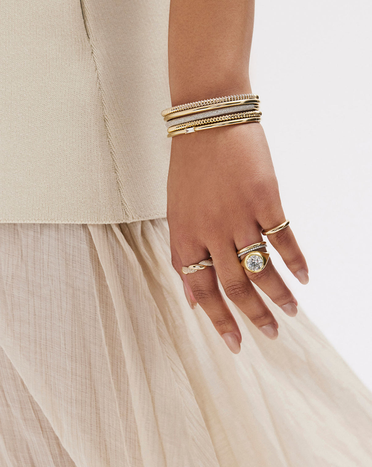 Slim Stackable Gold Cloud Bangle bracelet in 14k yellow gold shown on model's wrist with other gold and diamond bracelets, styled with various rings on hand