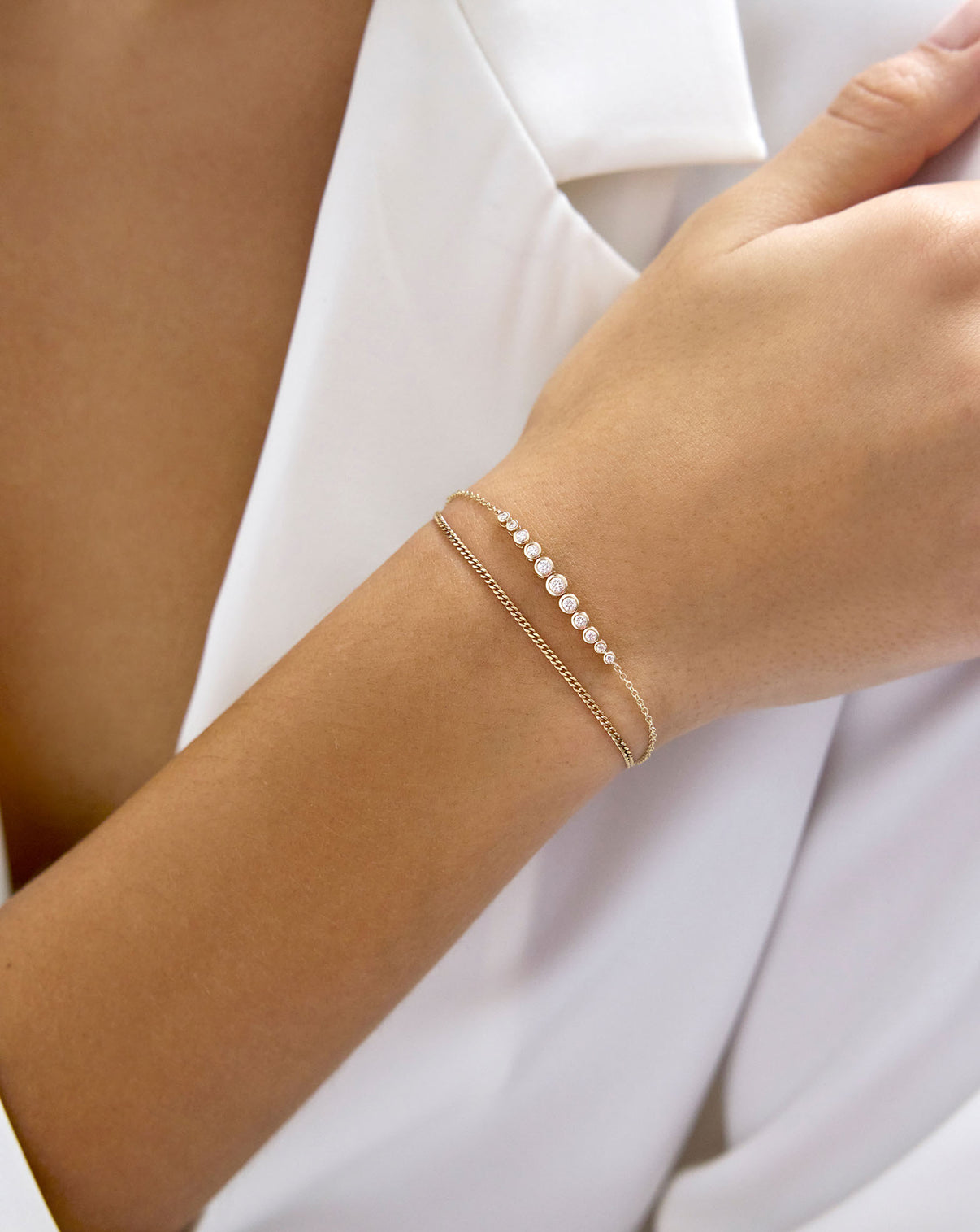 model wearing 14k Yellow Gold Graduated Diamond Bezel Soft Chain Bracelet styled with thin gold bracelet