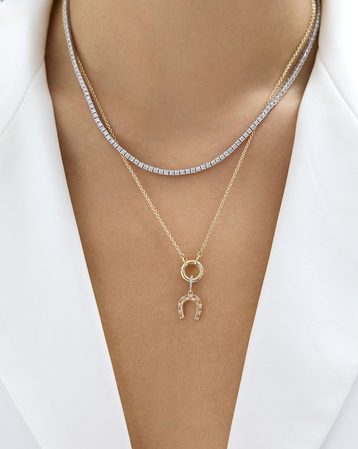 Horseshoe Charm on gold necklace and stacked with diamond tennis necklace on model