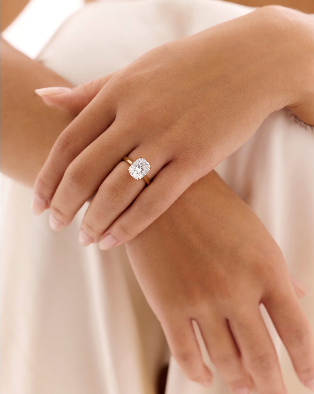 Model wearing 4.05 carat cushion cut lab-grown diamond engagement ring with cathedral-style yellow gold band, arms crossed at wrist