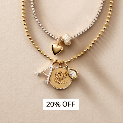 charms styled onto a tennis necklace and bead chain necklace against a travertine background