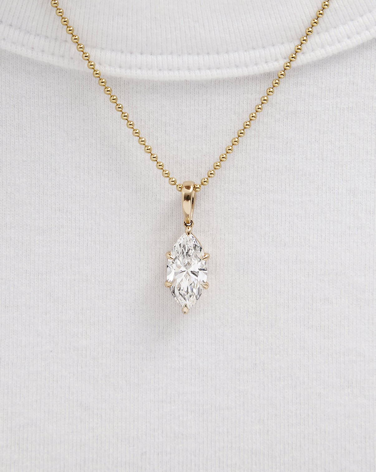 A gold chain necklace with a marquise-cut pendant, displayed on a white ribbed knit top.