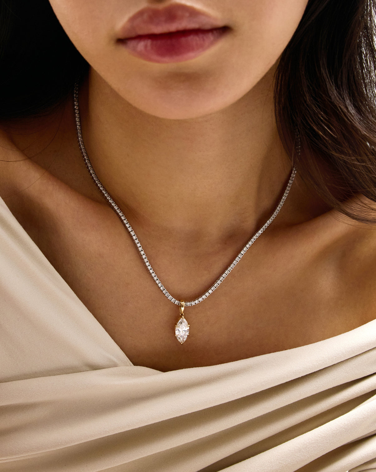A close-up of a model wearing a delicate diamond chain necklace with a marquise-cut pendant and gold-toned settings.