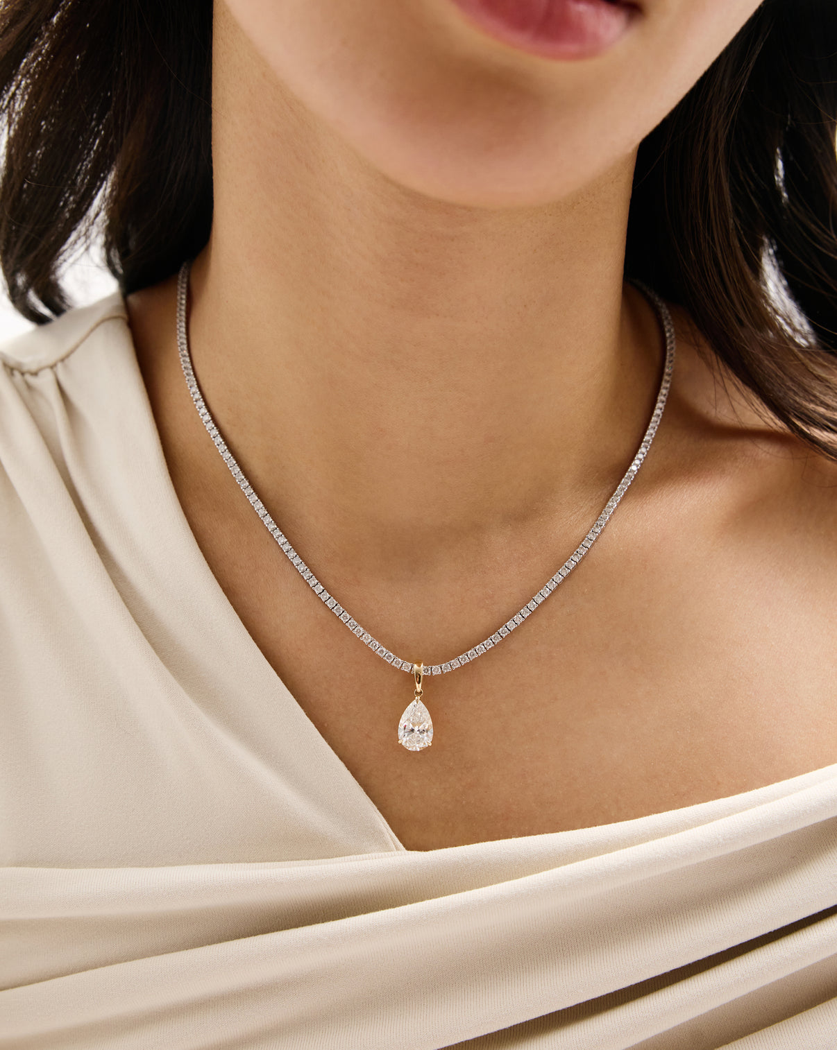 A close-up of a model wearing a delicate diamond chain necklace with a pear-cut pendant and gold-toned settings.