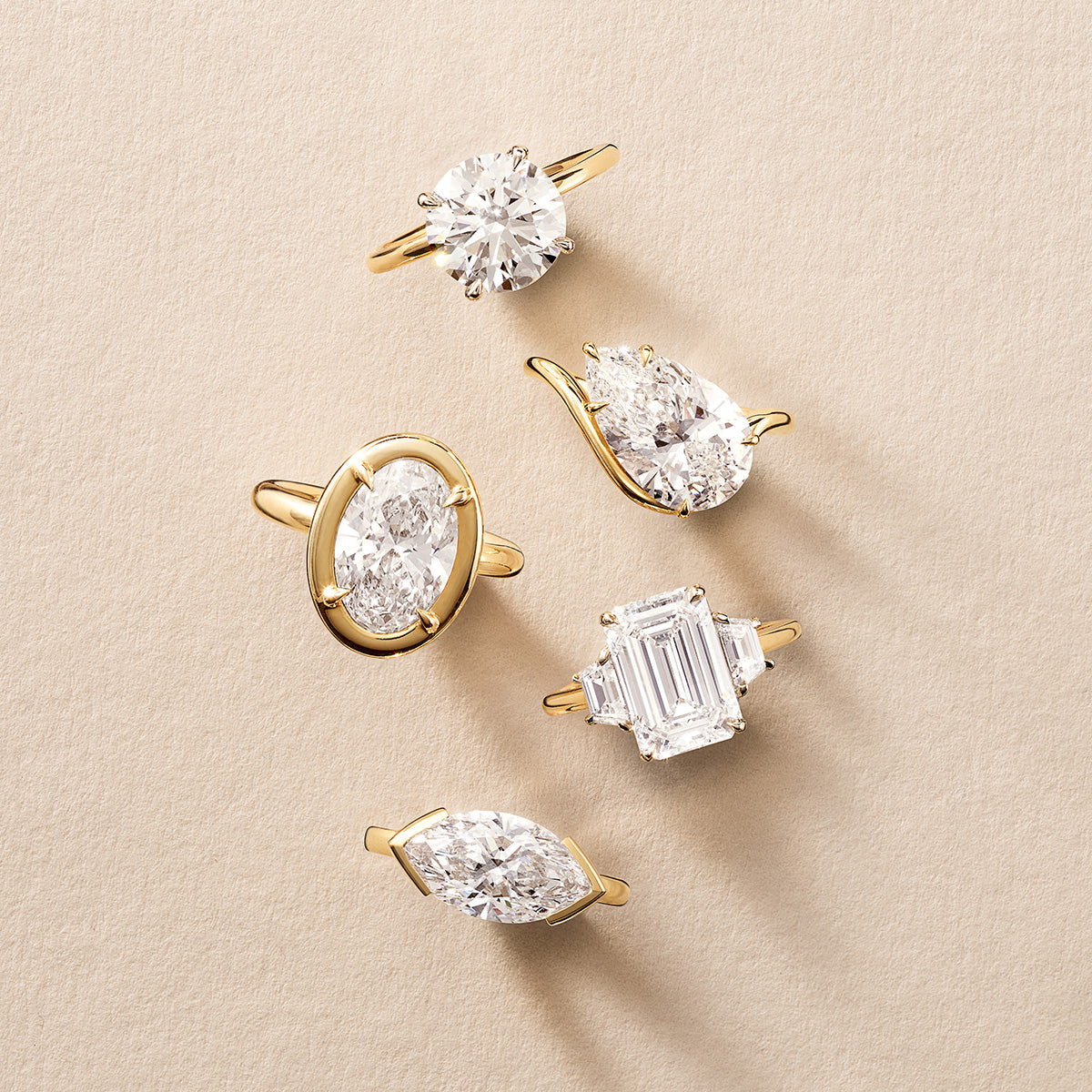 still life of 5 yellow gold engagement rings with different diamond shapes