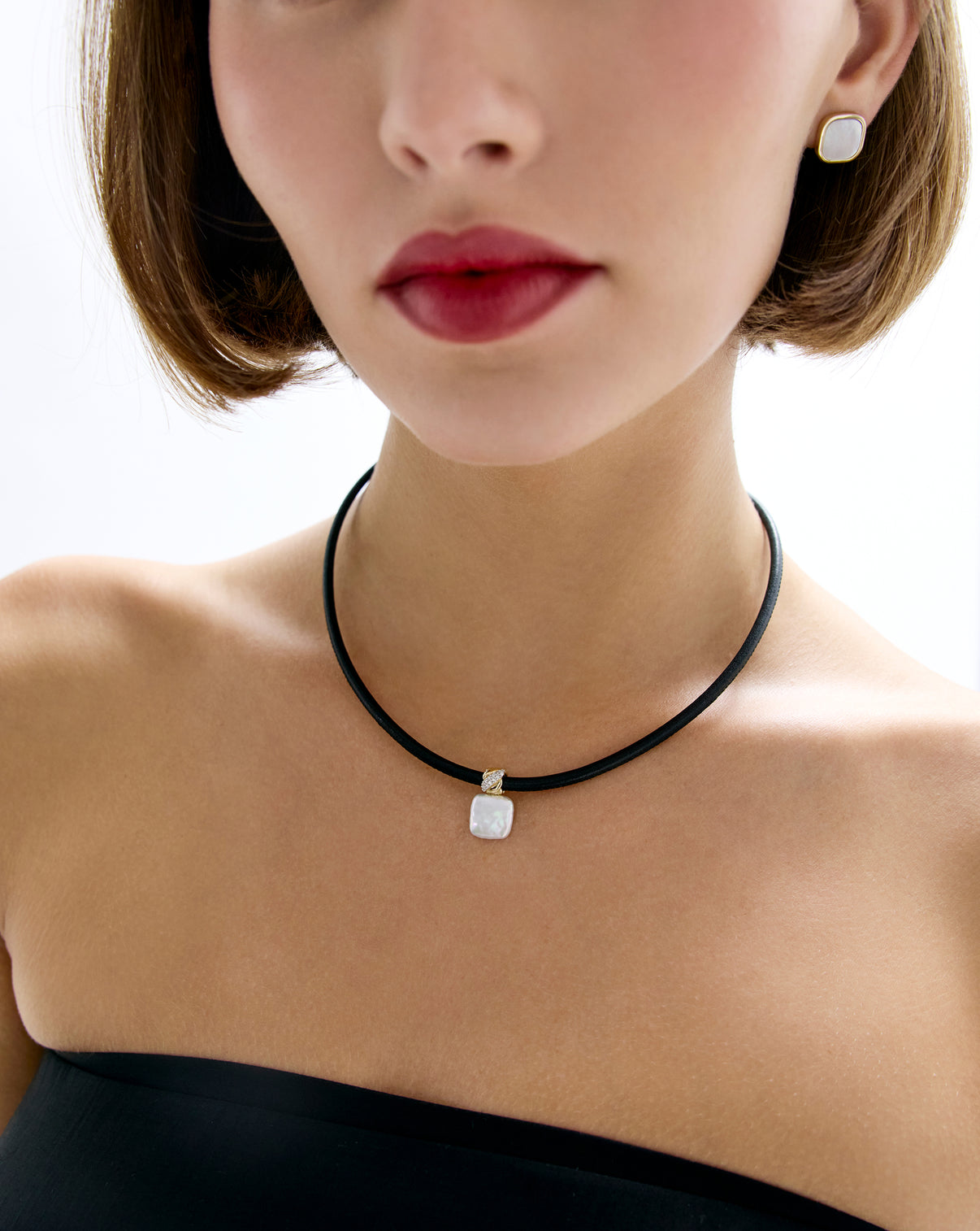 Model wearing leather cord necklace with square pearl pendant.