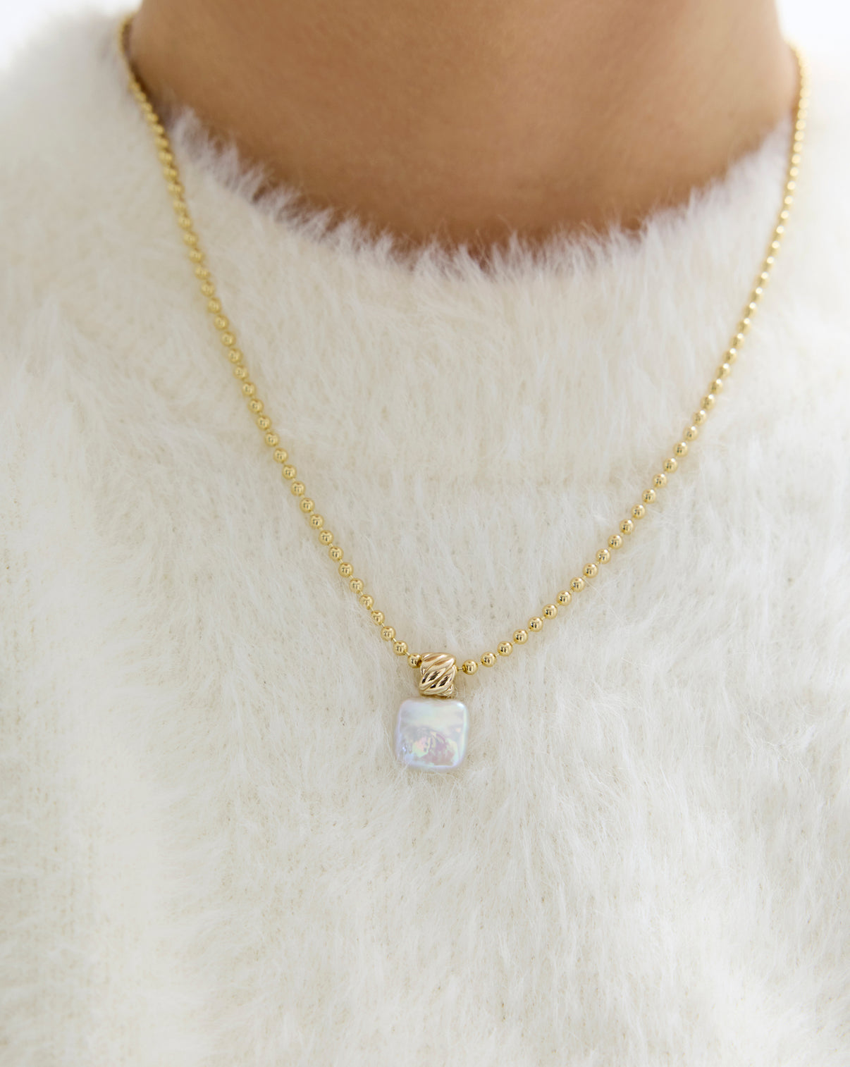 Close up of square pearl pendant being worn on gold chain.