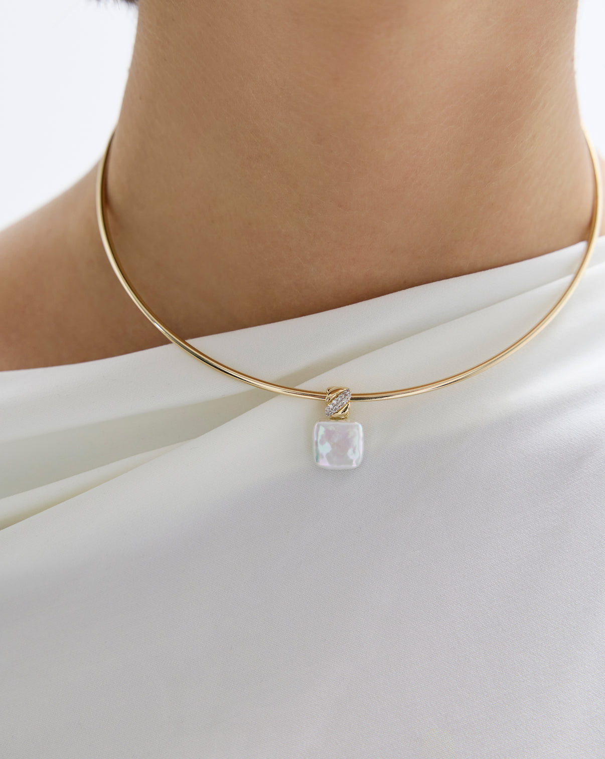 Close up view of model wearing square pearl pendant with gold necklace.
