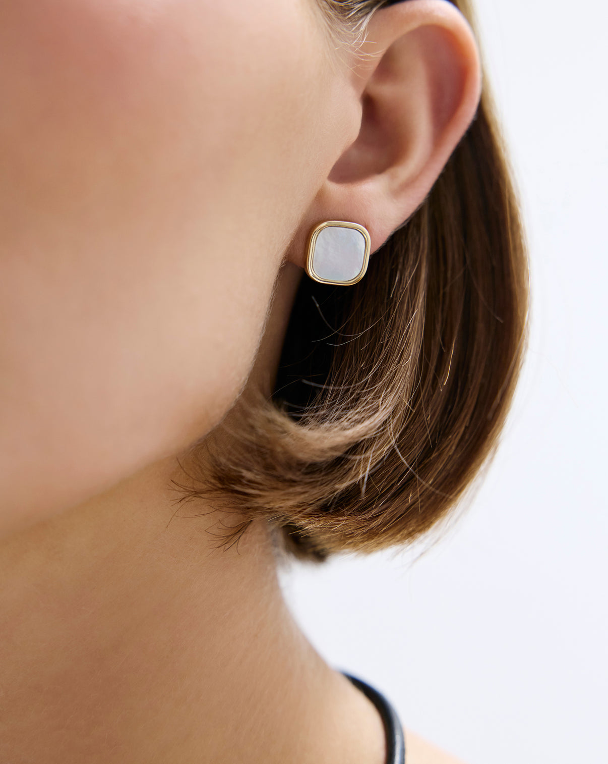 Close up view of square pearl earrings being worn as minimal studs with jacket removed.