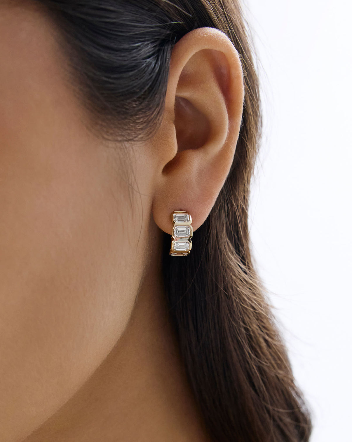 Detailed view of 14k solid gold 4 stone lab diamond bezel emerald huggies worn on ear