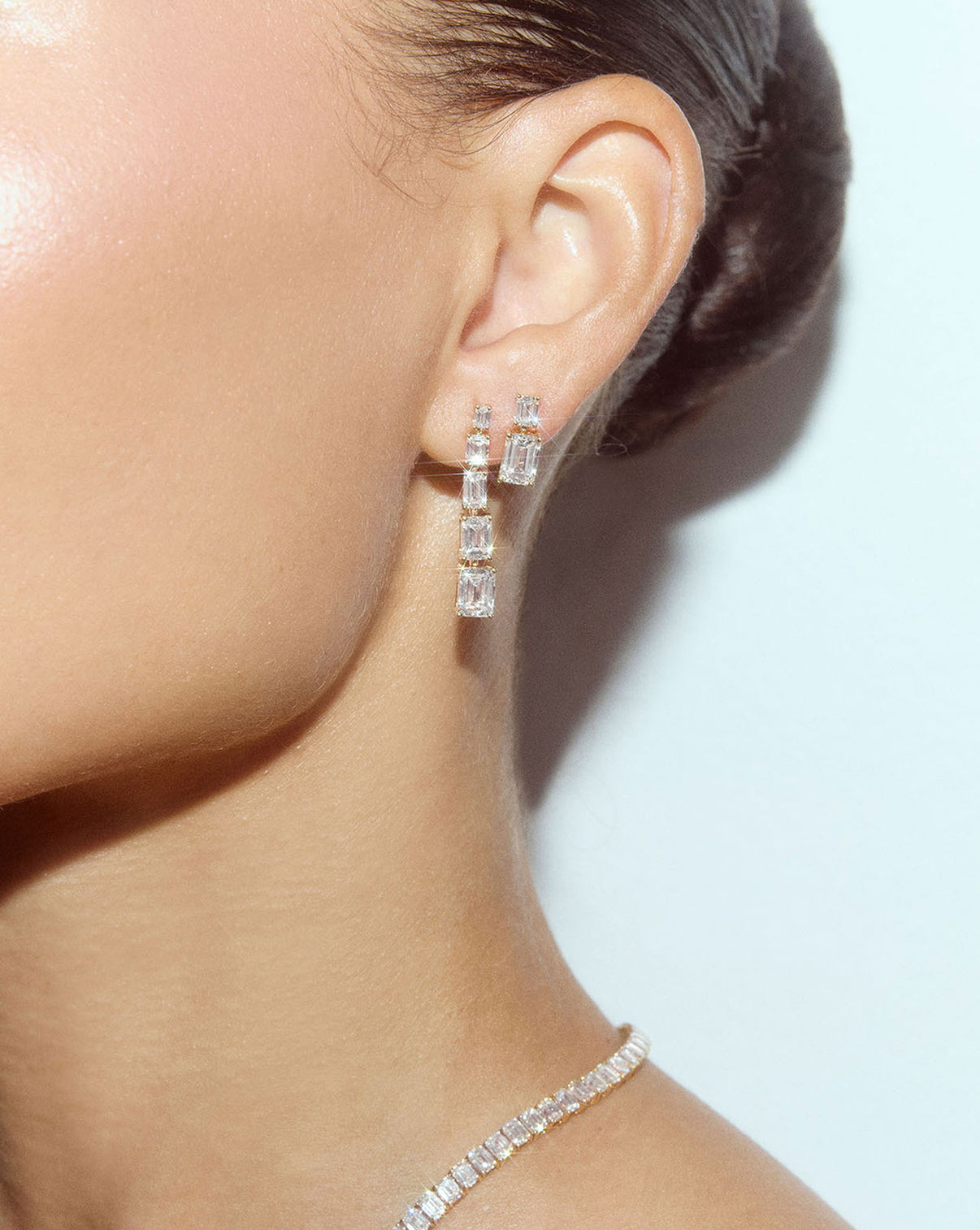 Close up view of emerald lab diamond drop earrings worn on ear
