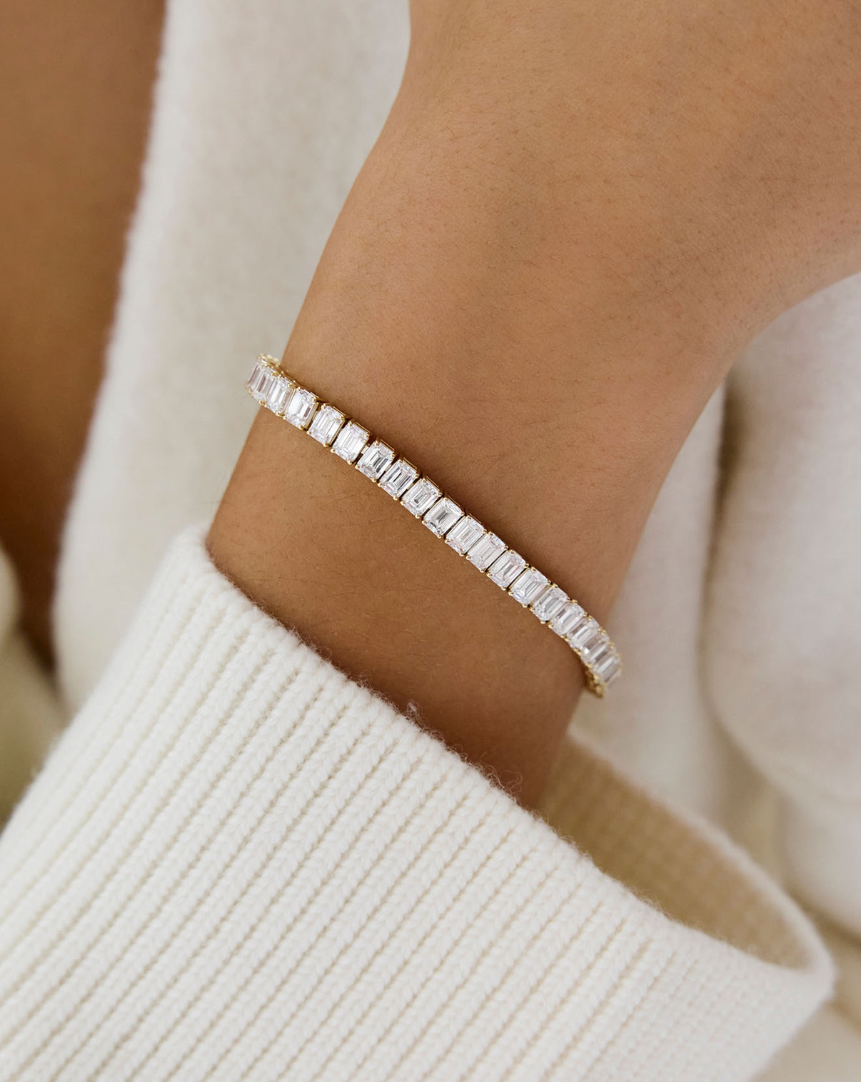Close up view of emerald lab diamond 14k gold tennis bracelet being worn on wrist