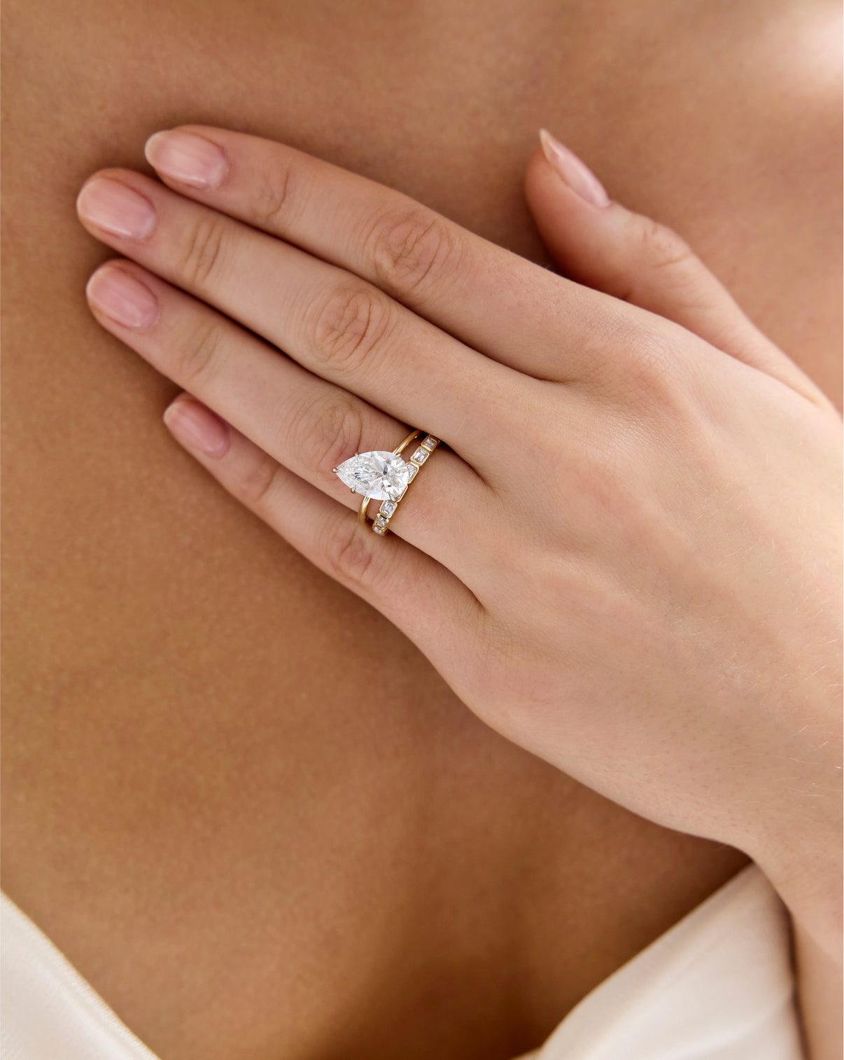 Model wearing Sideways Emerald Bezel Eternity Band stacked with off-center Pear Engagement Ring set in Whisper Thin global